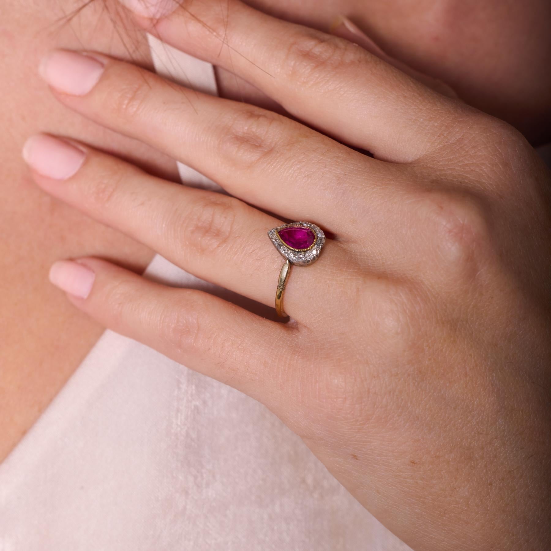 Romantique et raffinée, cette bague de style édouardien est centrée sur un rubis birman non traité dont la forme de poire et la teinte rouge pourpre brillent d'une rare beauté naturelle. Autour du rubis, dix-huit diamants de taille ancienne et de