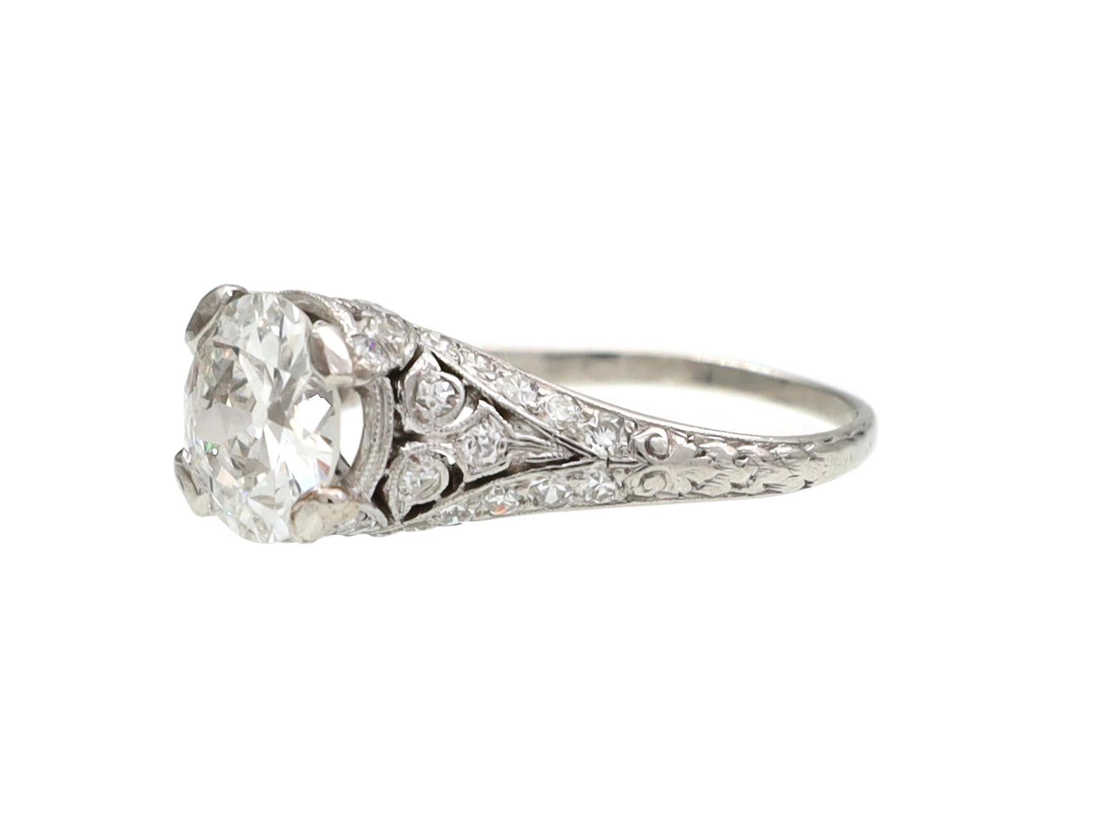 Edwardian solitaire engagement ring in platinum. Set with an estimated 1.22ct round Old European cut diamond, F colour, VS2 clarity in a raised four claw setting, to an elaborate solitaire design with diamond set collet, pierced openwork and