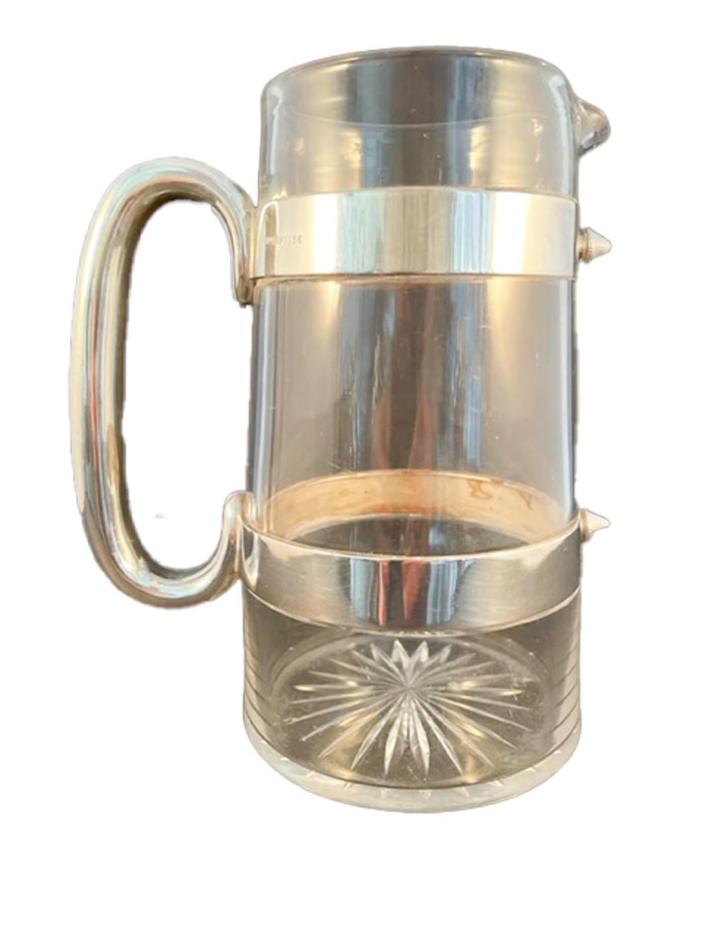 Edwardian clear blown glass water or cocktail pitcher of tapered cylindrical form with a molded lip and star pattern cut on the bottom. The 'C' shaped silver plate handle is attached to the two silver plate bands, which are closed at the front with