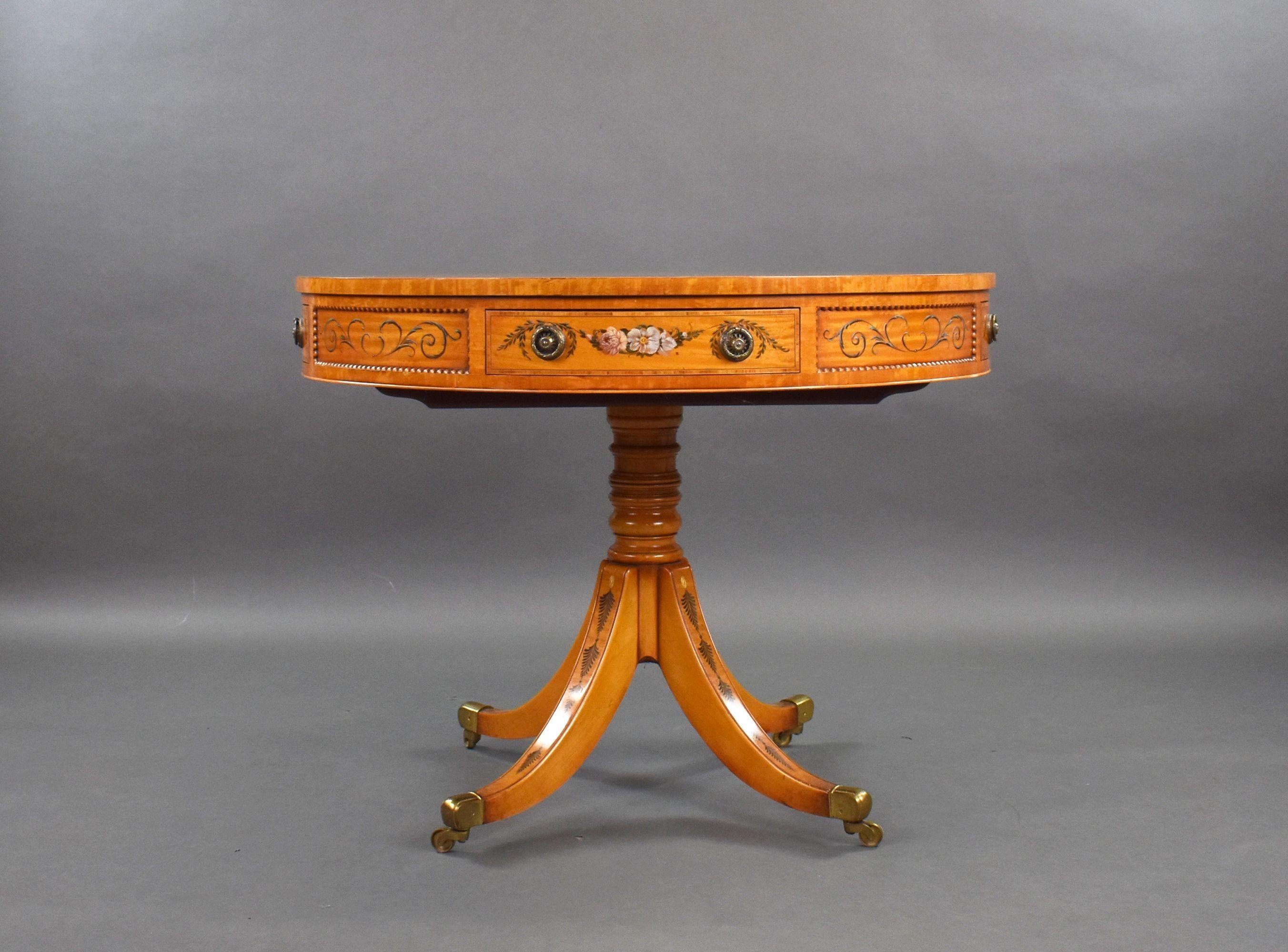 Il s'agit d'une table de tambour en bois satiné de bonne qualité, peinte à la main et datant de l'époque édouardienne. Elle présente une décoration florale au centre et sur les bords du plateau, au-dessus de quatre tiroirs, sur une tige tournée