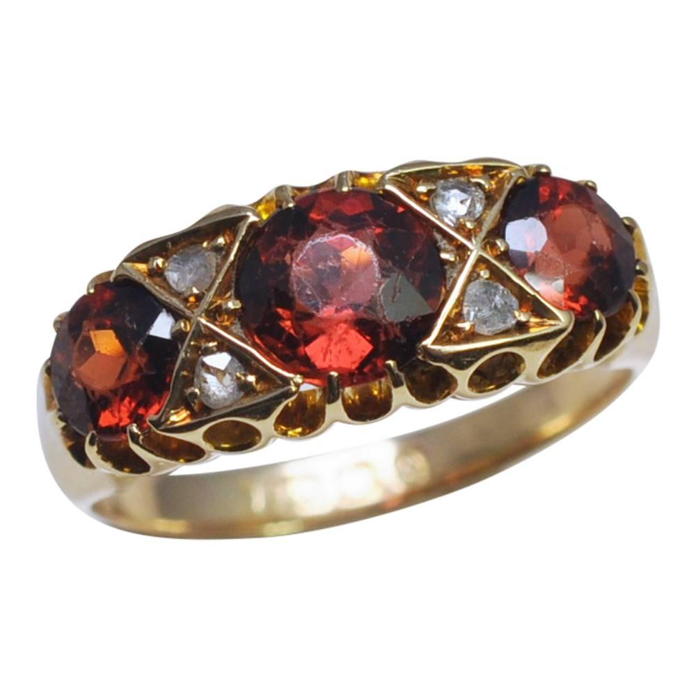 Edwardian garnet and diamond ring set in 18ct gold; the ring is in the classic antique English 3 stone design and set with three beautiful deep burnt orange garnets separated by rose cut diamond accents, all mounted over a pierced gallery.  This