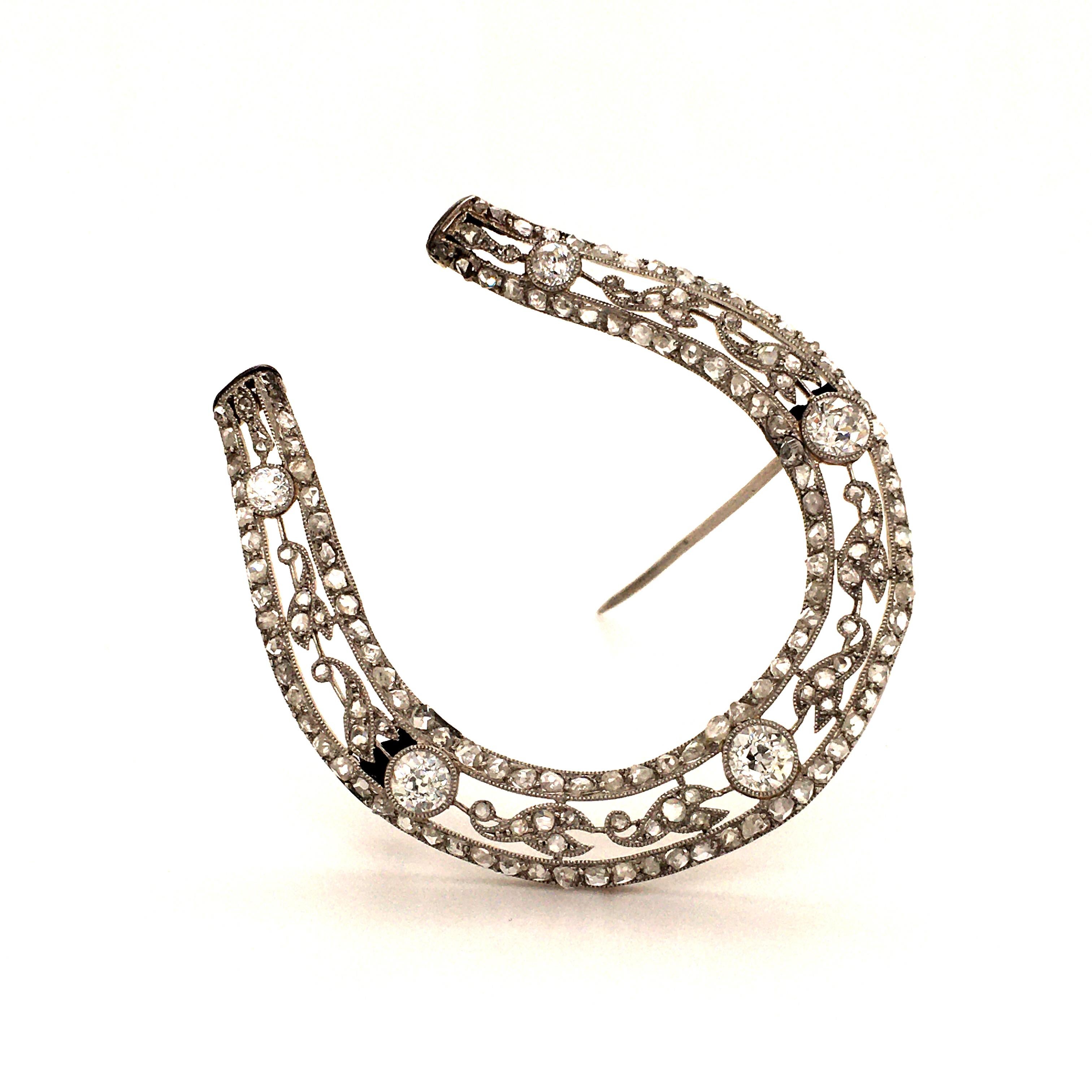 This delicate Edwardian horseshoe brooch is millegrain set with 5 Old European cut diamonds, total weight approximately 1.90 carats. The frame as well as the floral decorations are set with a charming mix of old rose cut diamonds of various