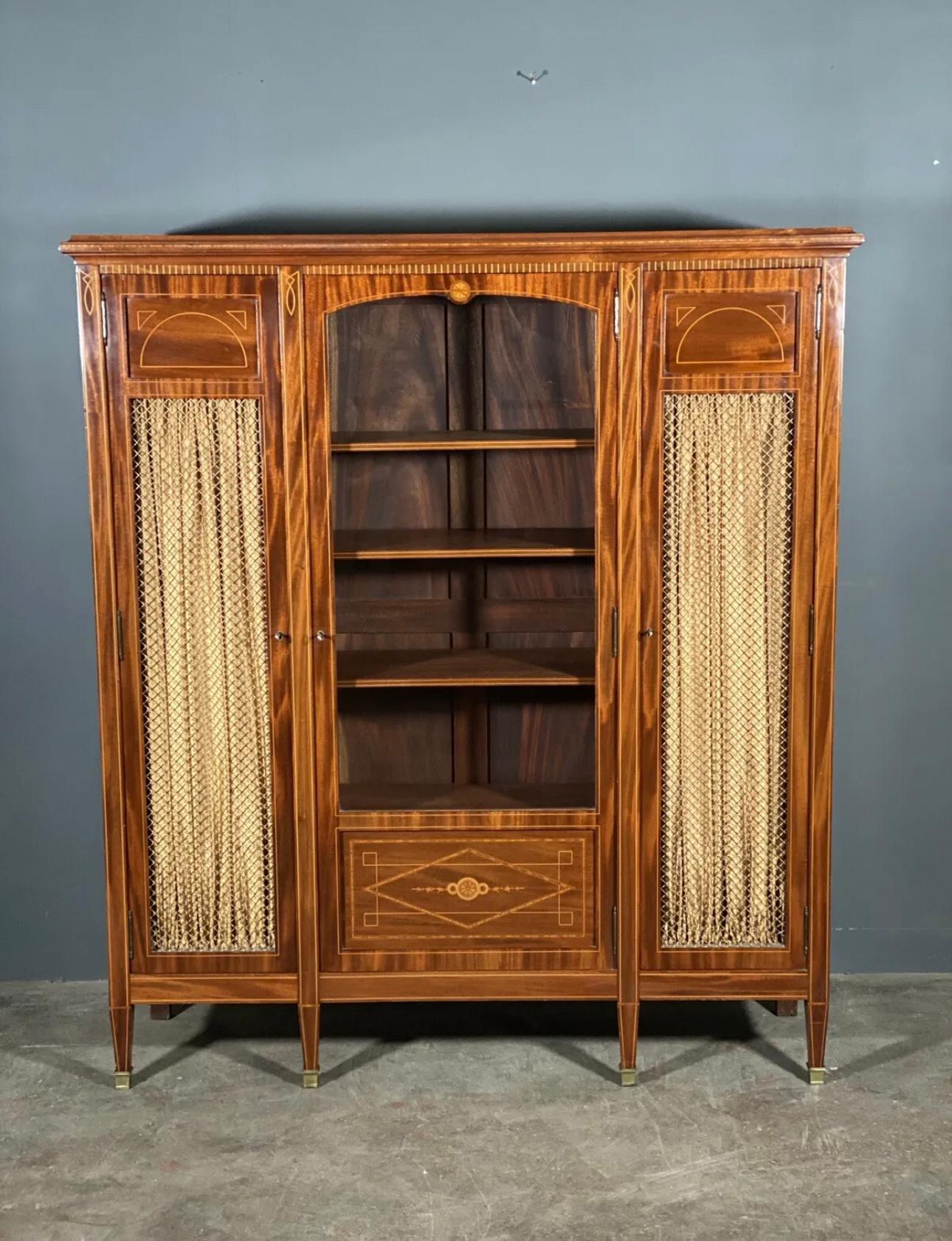 A fine quality display cabinet dating to the Edwardian period, The cabinet has two side cupboards with original brass grill and curtain, with a main glazed centre cupboard all of which have fully adjustable shelves. In very good condition with each