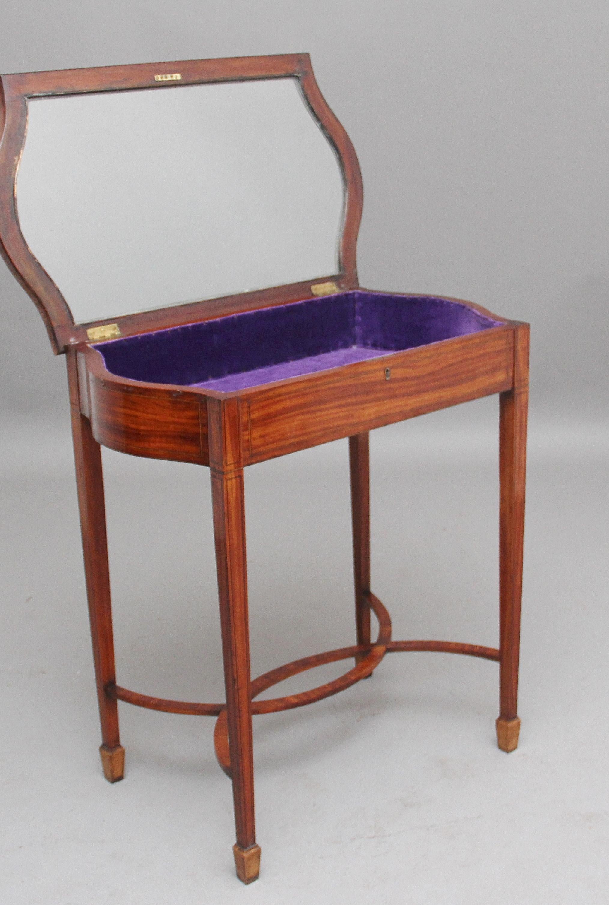 Early 20th century inlaid satinwood bijouterie / display table, the hinged lift up shaped glazed top opening to reveal the display area with a purple velvet lining inside, the top having shaped ends and decorated throughout with inlay, supported on