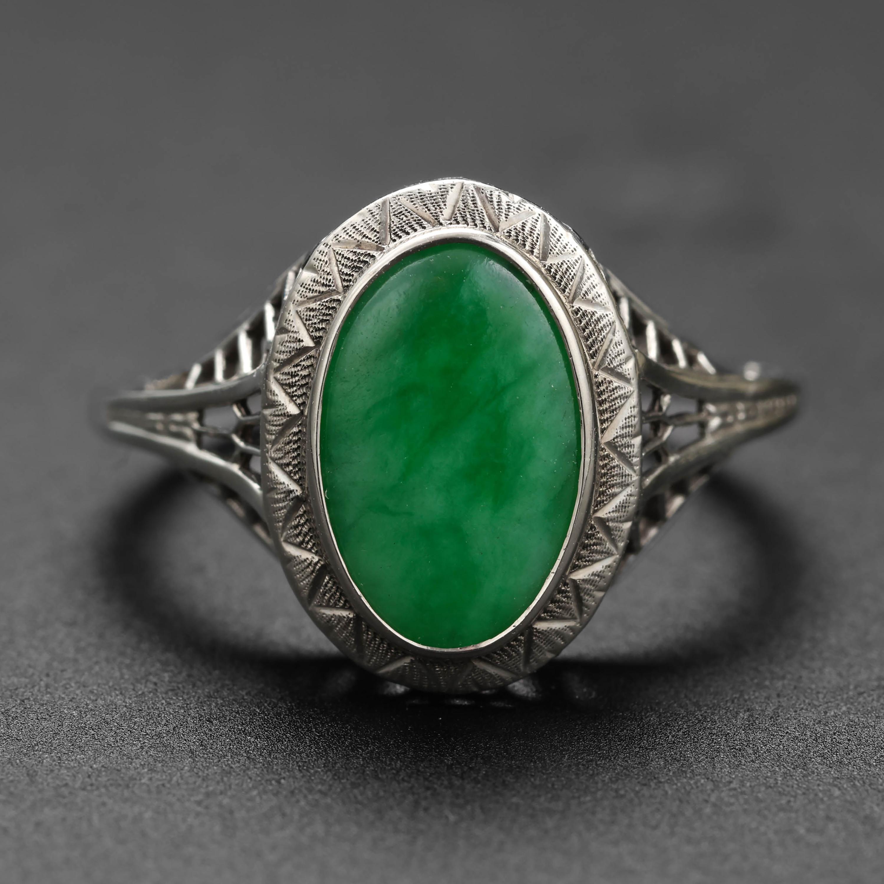 A luscious, translucent mottled emerald-green jadeite jade double cabochon is set within a highly detailed 18K white gold mounting in this Edwardian-era (circa 1905) ring. 

The jade stone measures 11mm x 7mm and has excellent translucency, as you