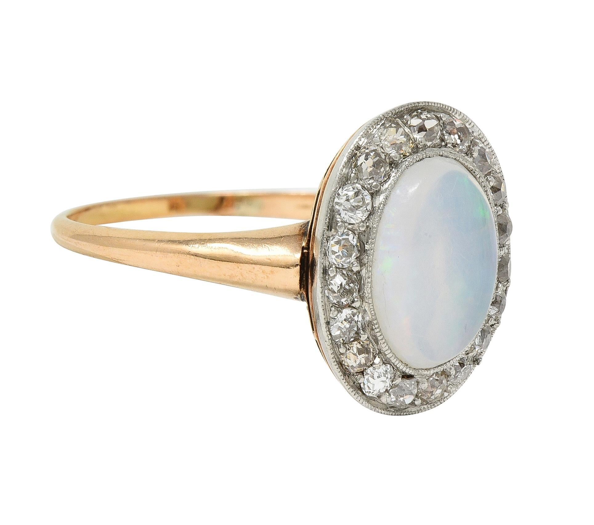 Centering an oval-shaped jelly opal cabochon measuring 10.0 x 8.0 mm 
Transparent white body color with spectral play-of-color 
Bezel set in platinum topped head with halo surround 
Comprised of old European and mine cut diamonds
Weighing