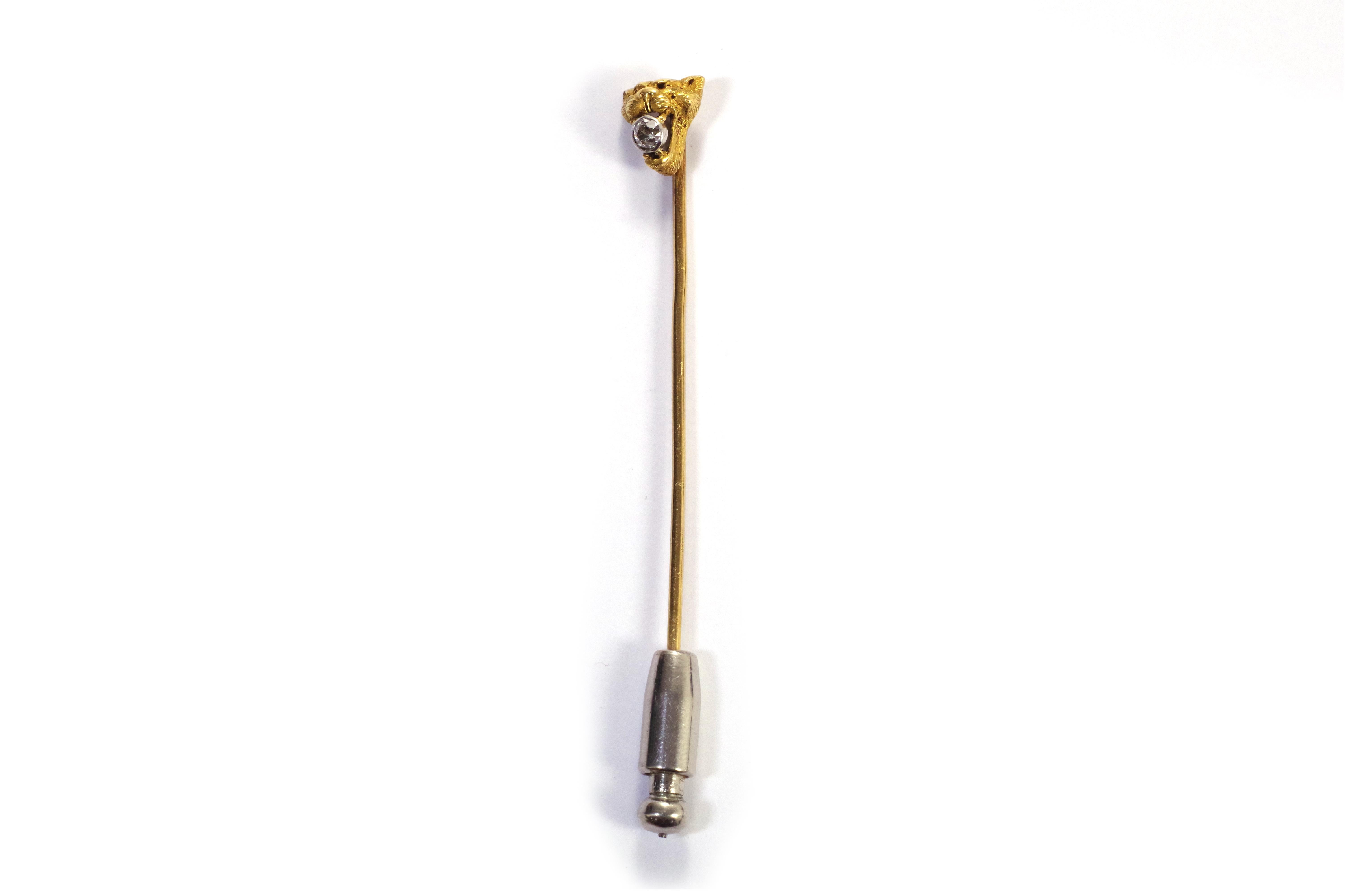 Edwardian lioness tie pin in 18-karat yellow gold and platinum. It features the head of a lioness with an open mouth, holding an old mine cut diamond set in a closed setting. The lioness's head is intricately detailed, showcasing its fur. The