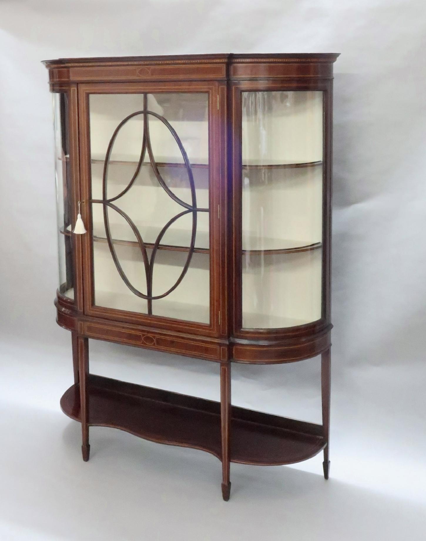 A very good quality Edwardian fiddle back mahogany bow ended glazed display cabinet with chequered and boxwood string inlay stood on square tapering legs and spade feet with shelf. The cabinet has a working lock and key.

Inside, the cabinet has