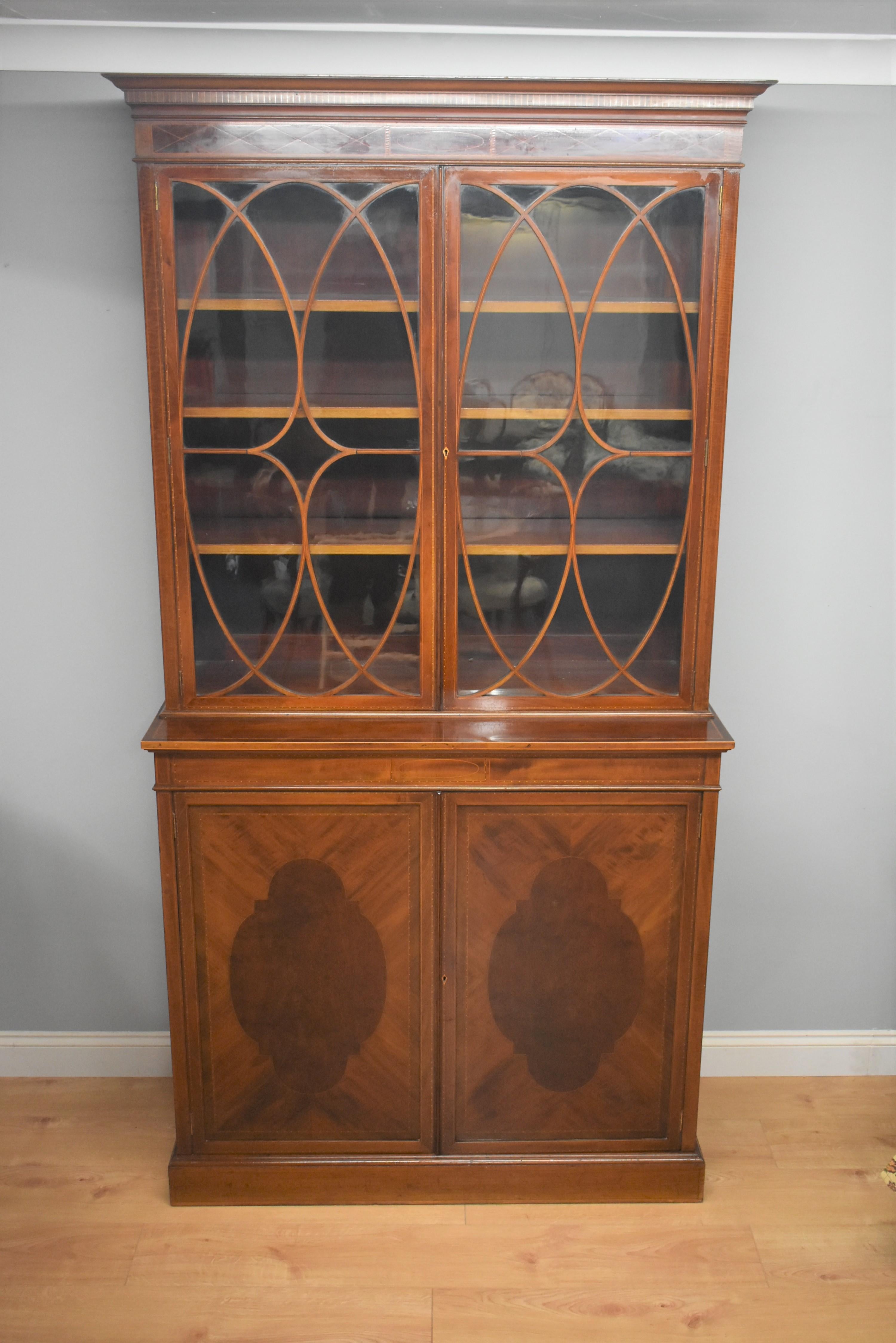 Edwardian mahogany and boxwood line inlaid bookcase, the upper section with adjustable shelves enclosed by astragal glazed doors, the projecting base enclosed by a pair of panelled cupboard doors on a plinth base. In good condition. Dismantles top