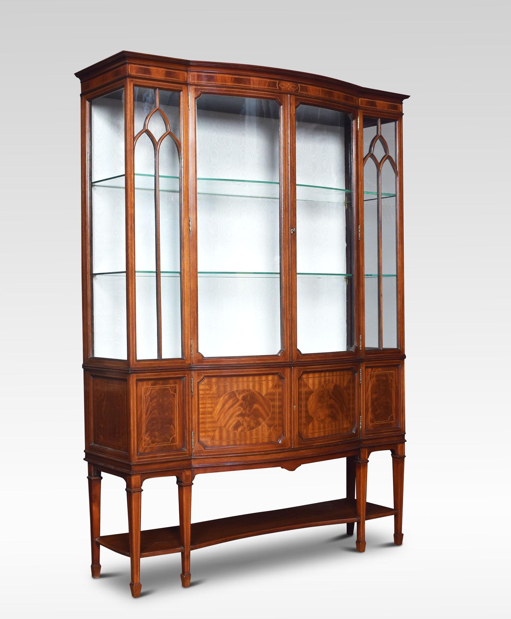 Edwardian mahogany bow front display cabinet. Having a pair of astragal glazed centre doors enclosing shelved and watermark silk upholstered interior, flanked by glazed ends, with a pair of cupboard doors below. All raised up on reeded tapering