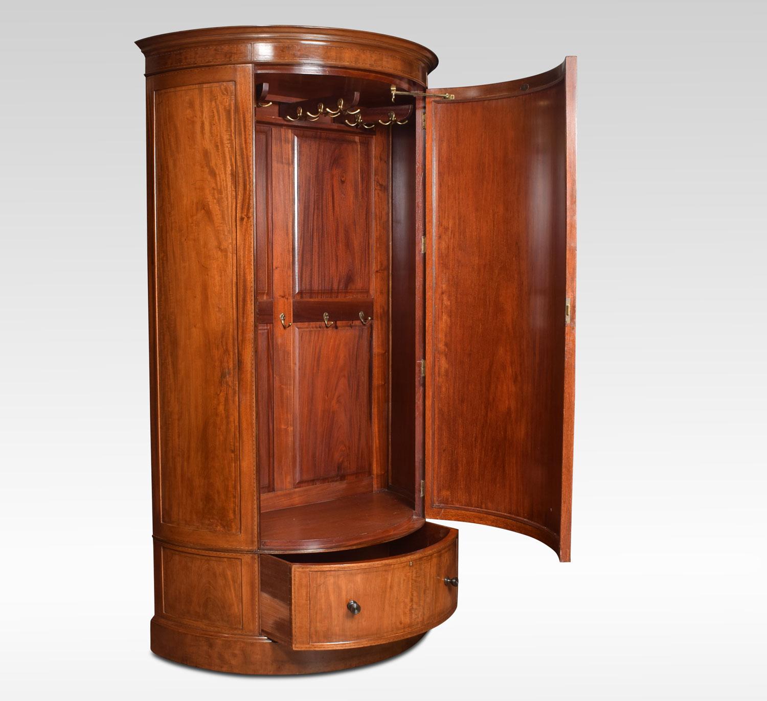 Edwardian mahogany bow front wardrobe. The moulded cornice above large curved oval panelled door. Opening to reveal the interior having an arrangement of swivelling hanging hooks. The base fitted with single draw with turned knob handles. All raised