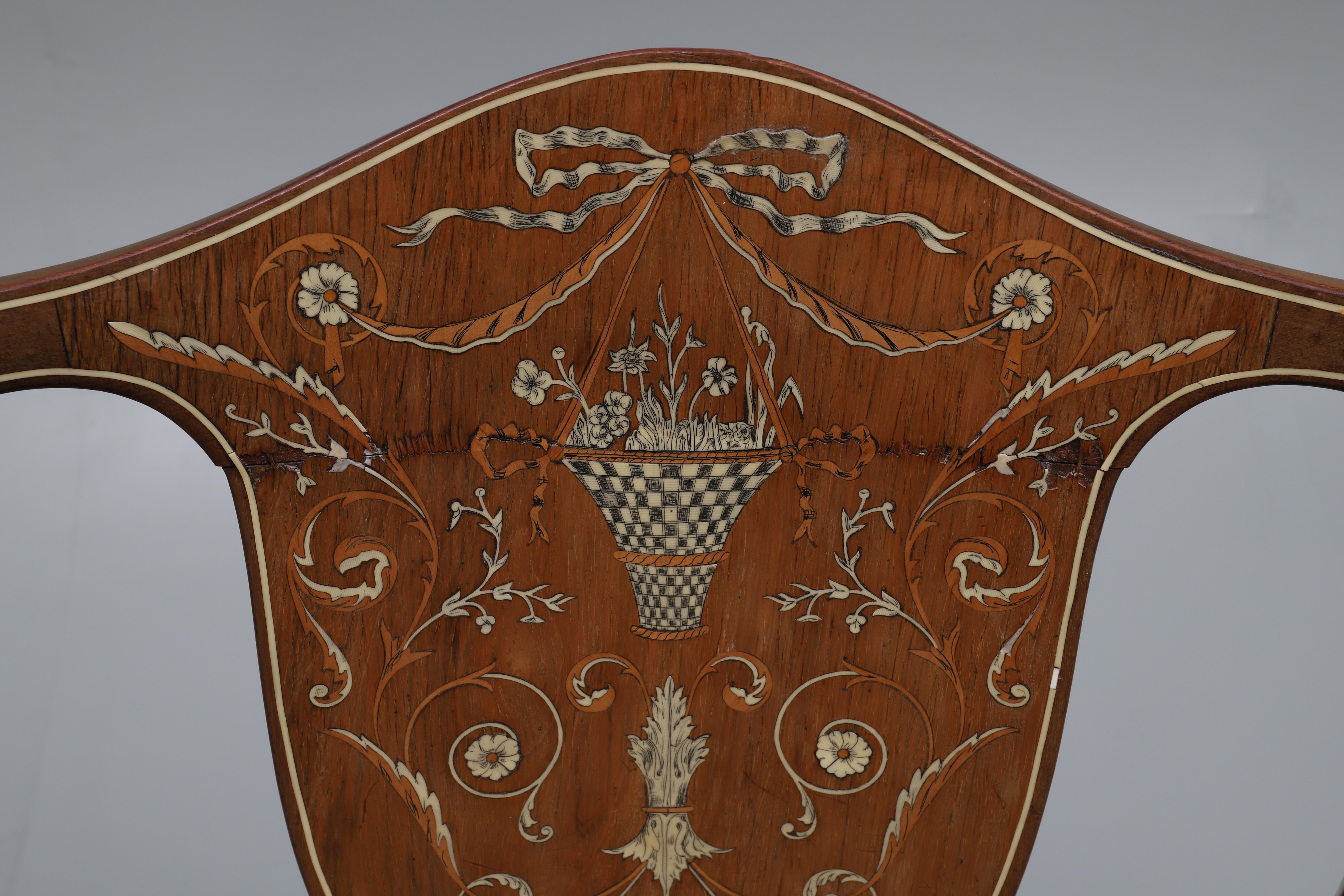 The shaped curved back with a central hardwood panel inlaid with a ribbon tied hanging basket of flowers surrounded by flowering and scrolling branches, having an upholstered seat, on square tapering legs with spade feet, measures: 55cm wide x 48cm
