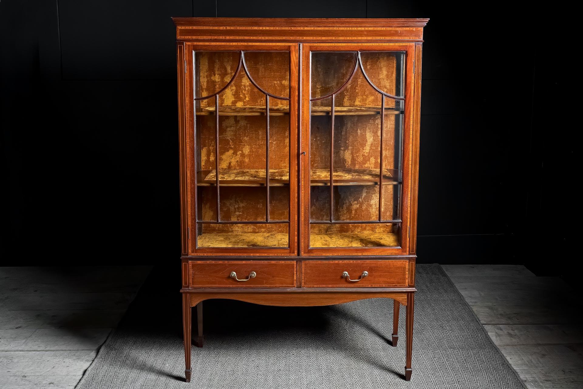 Exemple exquis de l'artisanat anglais du début du XXe siècle, cette vitrine édouardienne - datant d'environ 1908 - est façonnée dans un acajou aux tons chauds et ornée d'un travail de marqueterie finement exécuté qui encadre délicatement sa forme