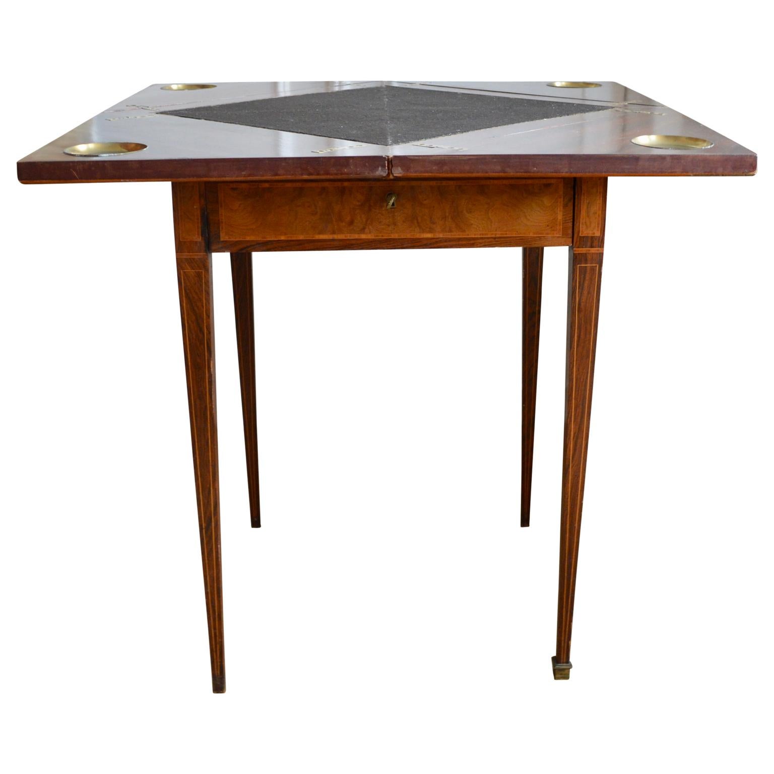This Edwardian mahogany envelope card table, circa 1900 is a very unique design with a beautifully figured top with crosssbanded satinwood edge. The top swivels and four sections open up to reveal a black felt playing surface and four counter wells.