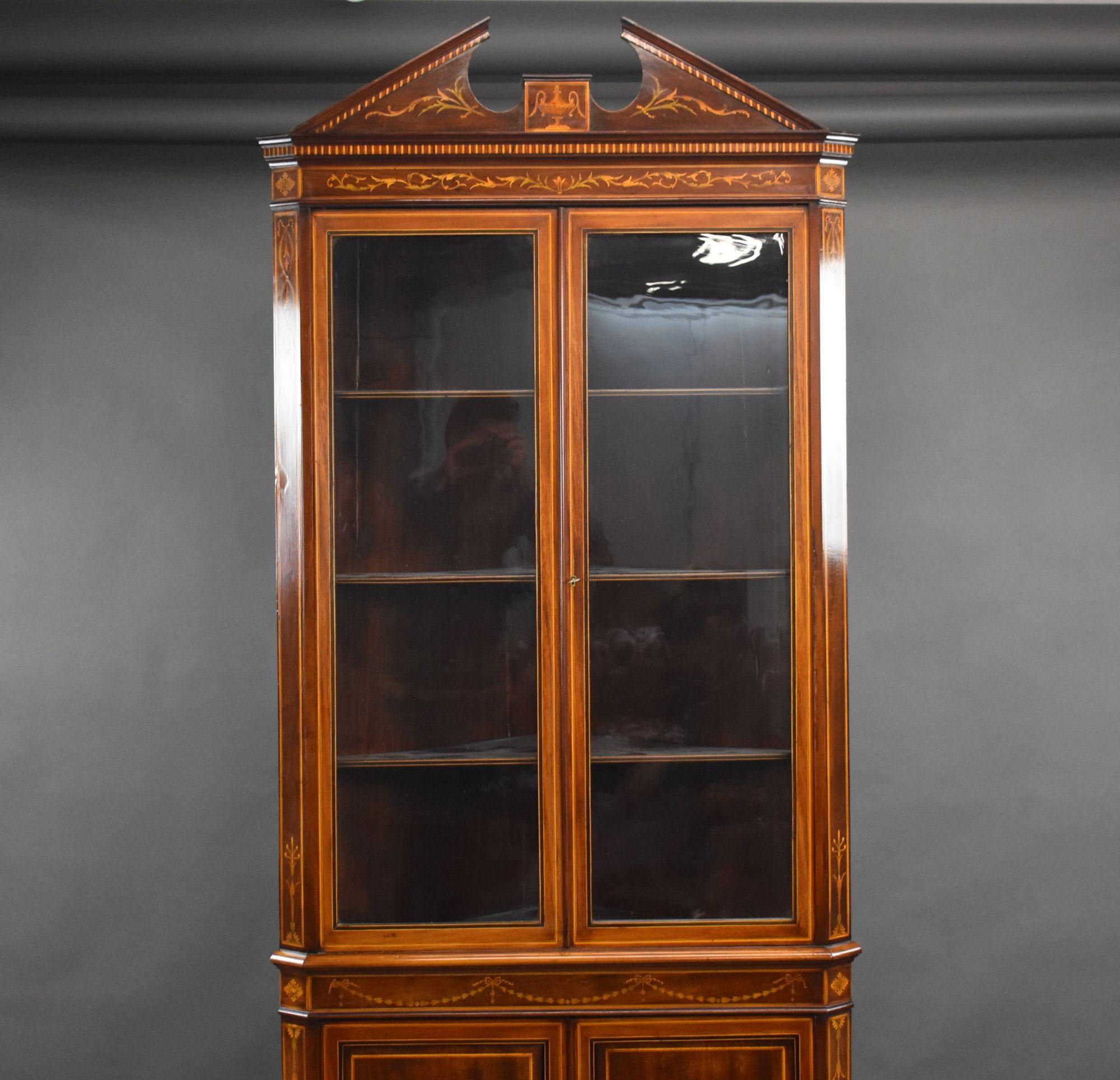 For sale is a top quality Edwardian inlaid corner cabinet, having an inlaid broken arch pediment, above two glazed doors opening to reveal a single removable shelf, above two cupboard doors, each finely inlaid with marquetry. The cabinet stands on