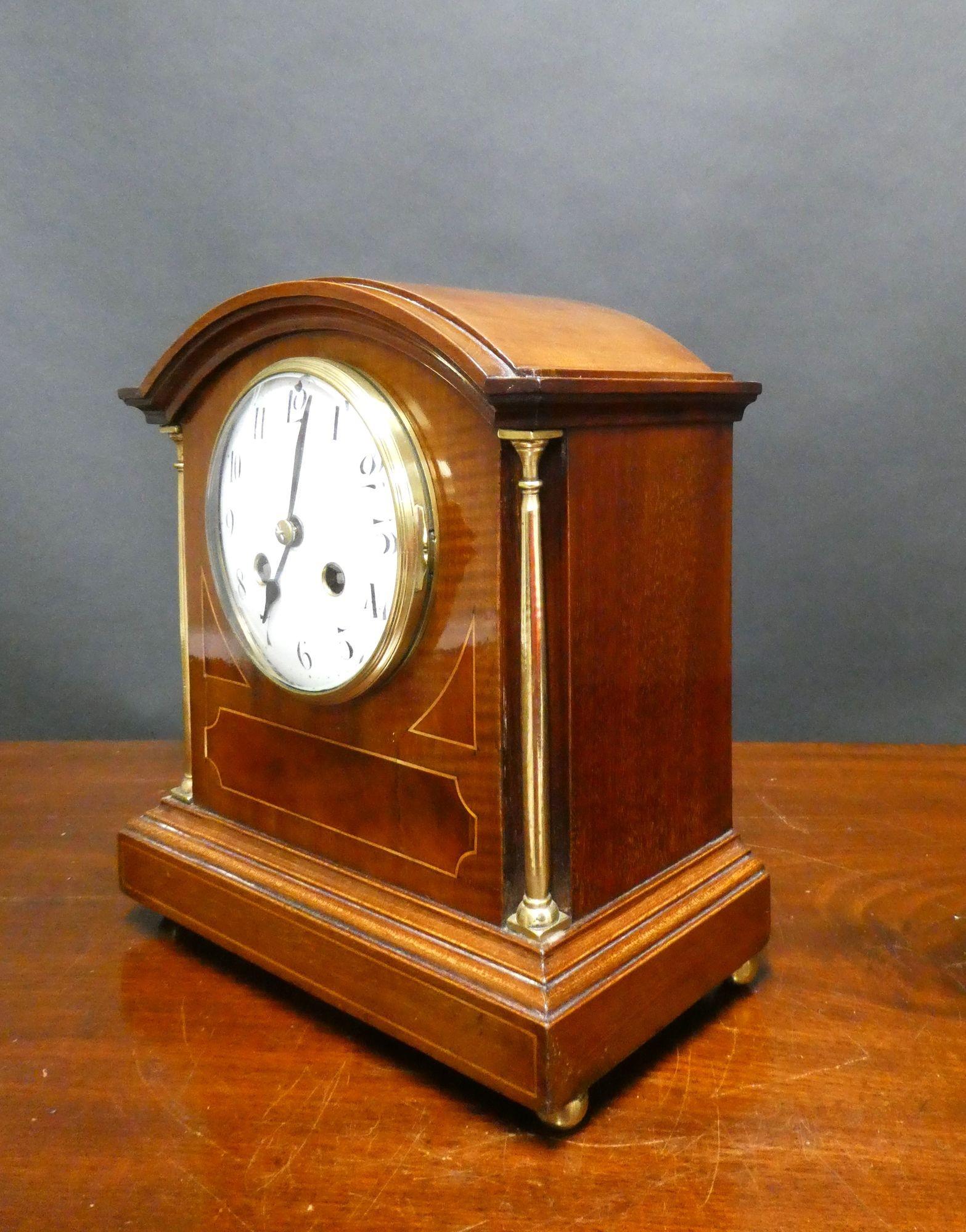 Edwardian Mahogany Inlaid Mantel Clock

Edwardian mantel clock housed in a break arch mahogany case with walnut panels and satinwood line stringing , brass pillars to either side with a stepped plinth resting on four brass bun feet.
Brass bezel with