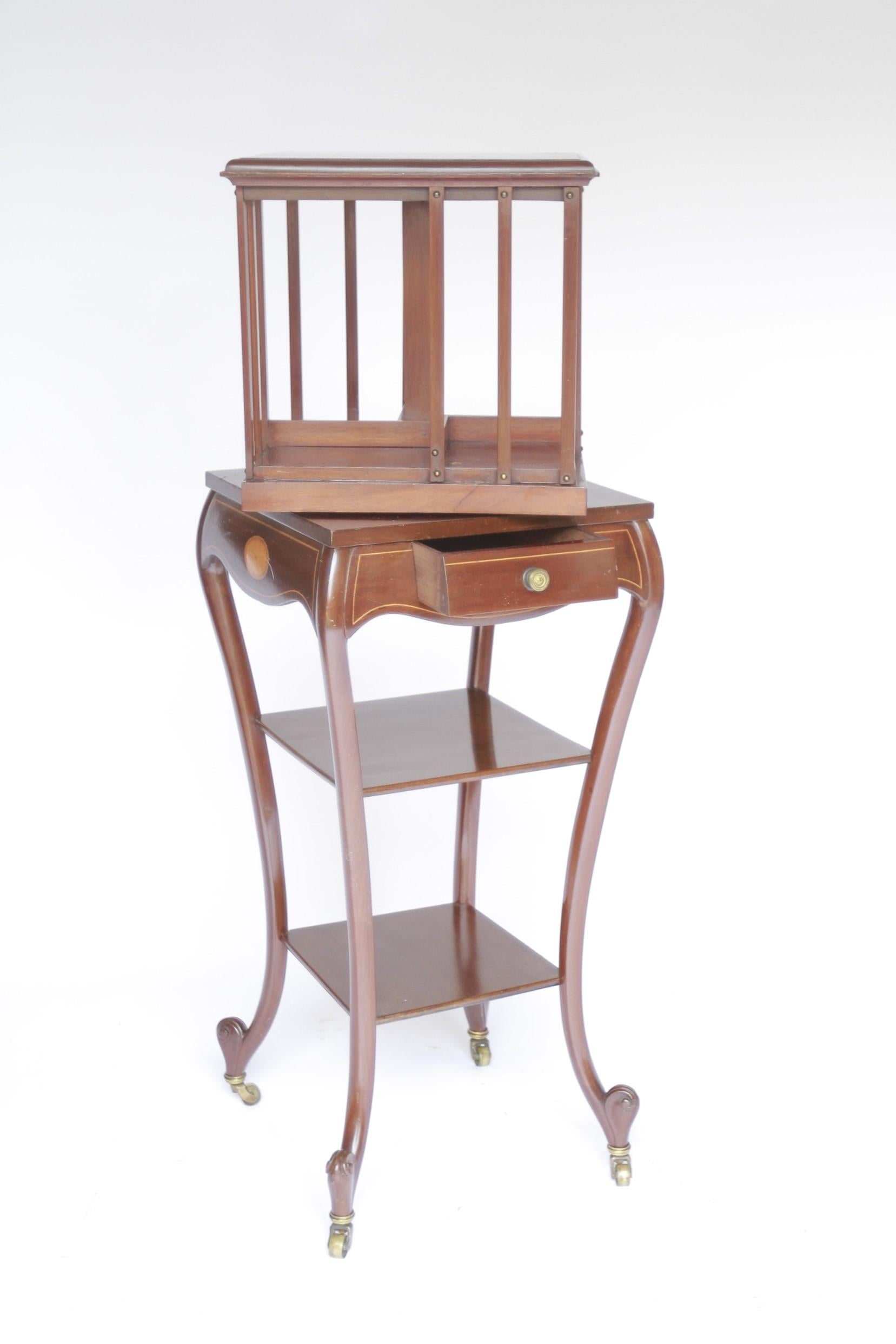 Square top with circular inlaid centre.
4 inlaid Fans to each corner
Revolving top with 4 open sections to hold books
Slatted Mahogany sides.
Shaped 2 tier base with single drawer at front. 
oval fan inlaid & boxwood line detail
Carved scroll feet