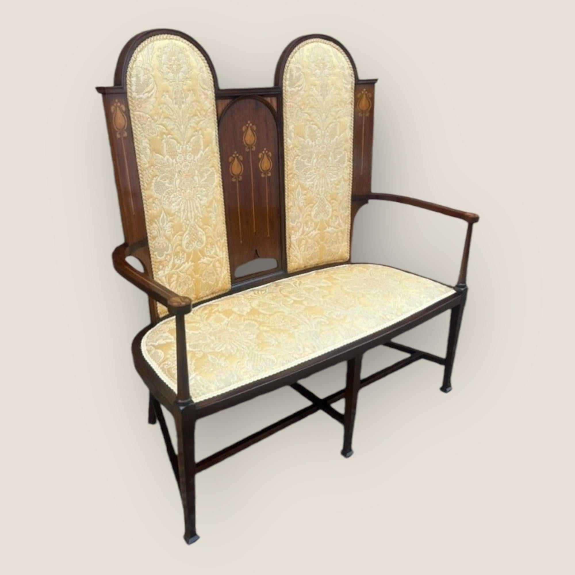 Divano imbottito con schienale ad arco alto in mogano e legno satinato intarsiato in stile Art Nouveau a due posti. Con un'imbottitura floreale dorata su supporti affusolati quadrati.