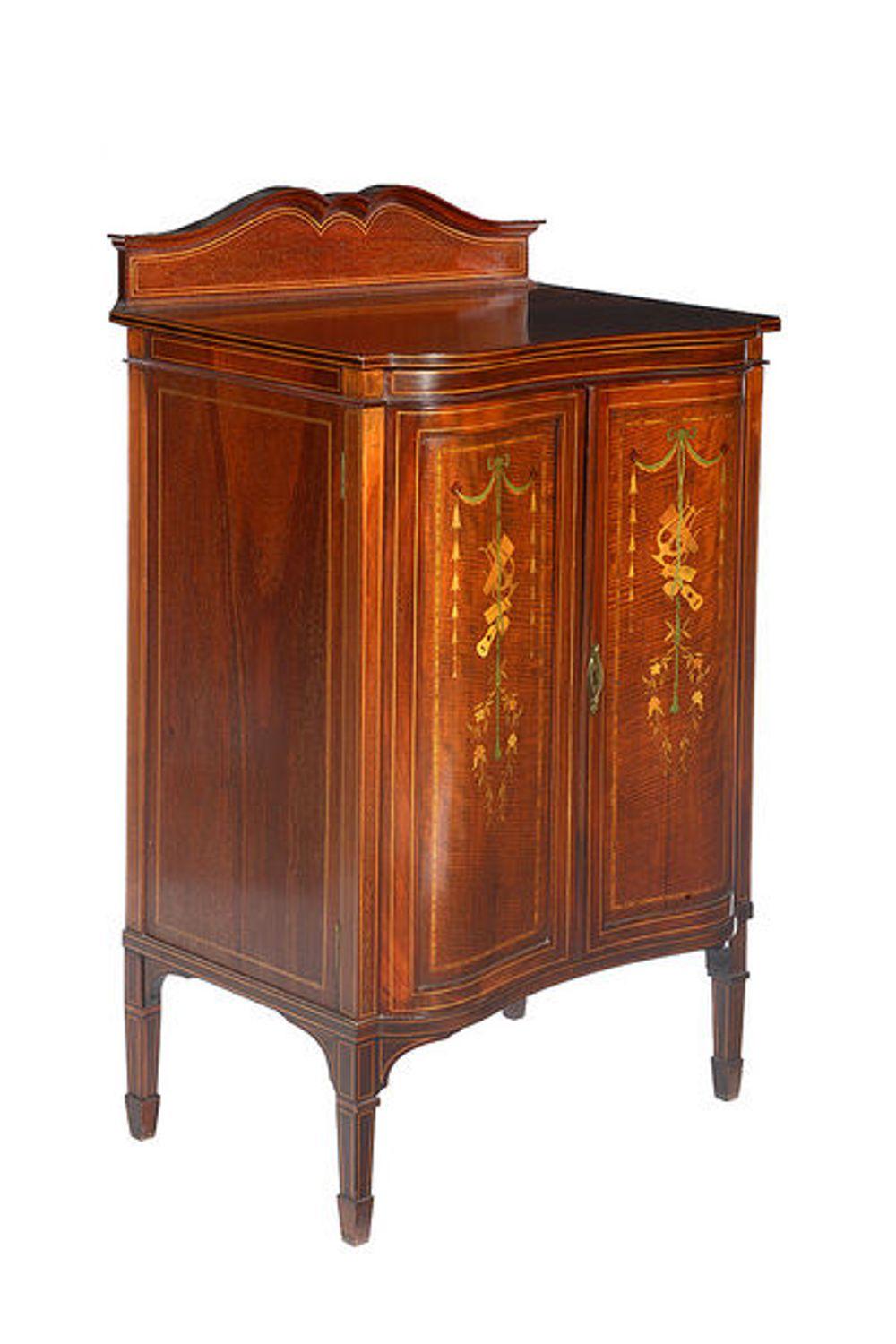 A mahogany and satinwood marquetry Edwardian two-door music cabinet.

The inverted serpentine shaped top with a raised back and a pair of arched cabinet doors inlaid with satinwood musical emblems, garlands and bell flowers. 

The doors open to