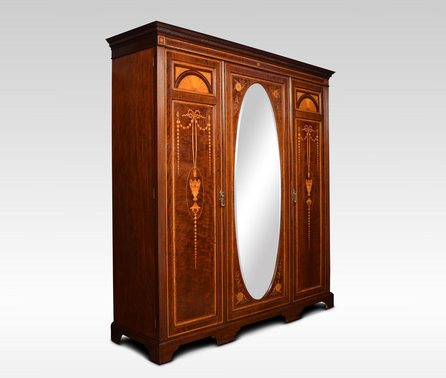 Edwardian mahogany three-door wardrobe the projecting cornice above centre oval beveled mirrored door opening to reveal linen trays and drawers. The trays can be removed to add additional hanging area. Flanked by a pair of floral marquetry inlaid