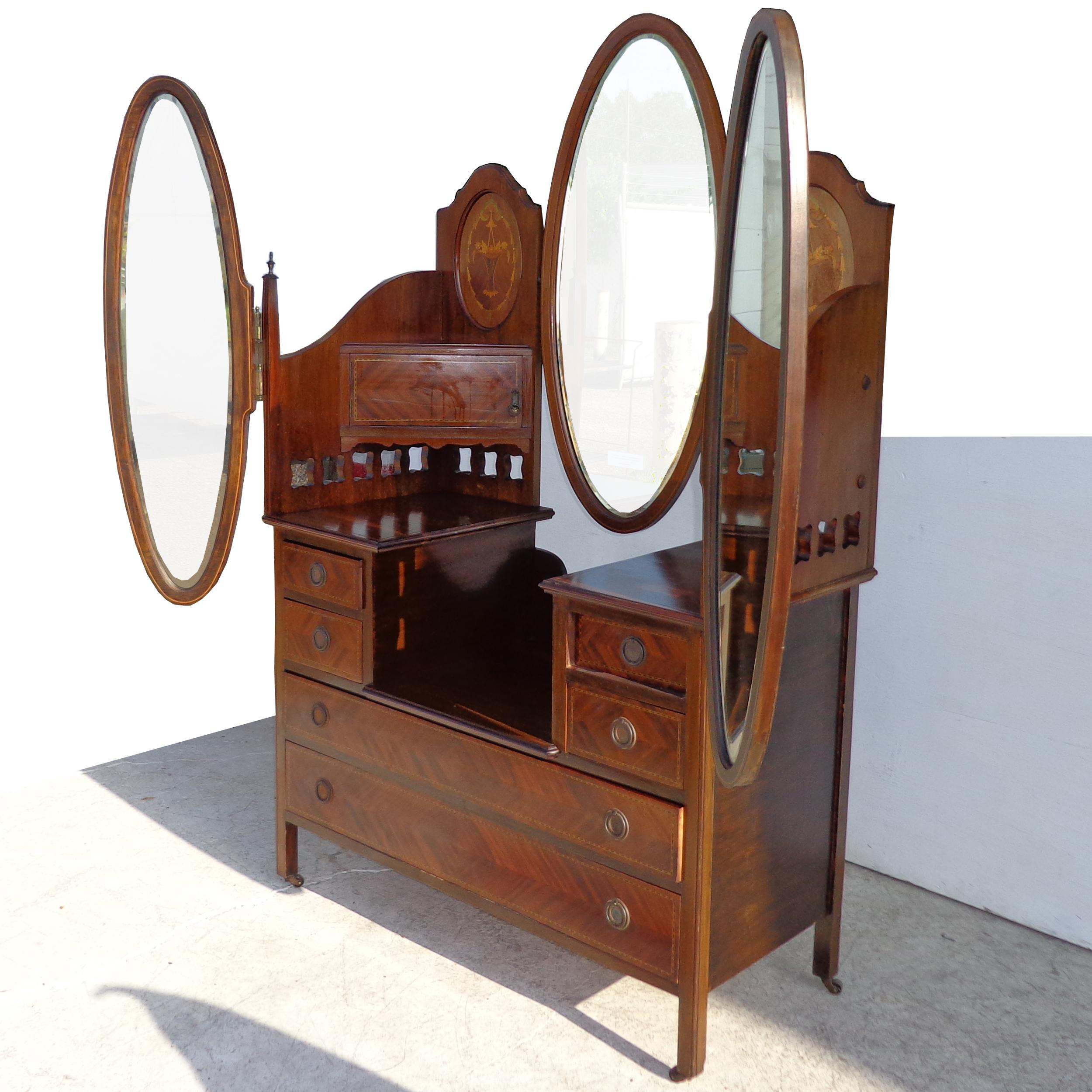 Mahogany triple mirror vanity with adjustable mirrors
1900s

This stunning vanity has a raised back with burled and parquetry oval panels. One center oval mirror flanked by 2 adjustable mirrors on each side.
Two concealed corner jewelry drawers