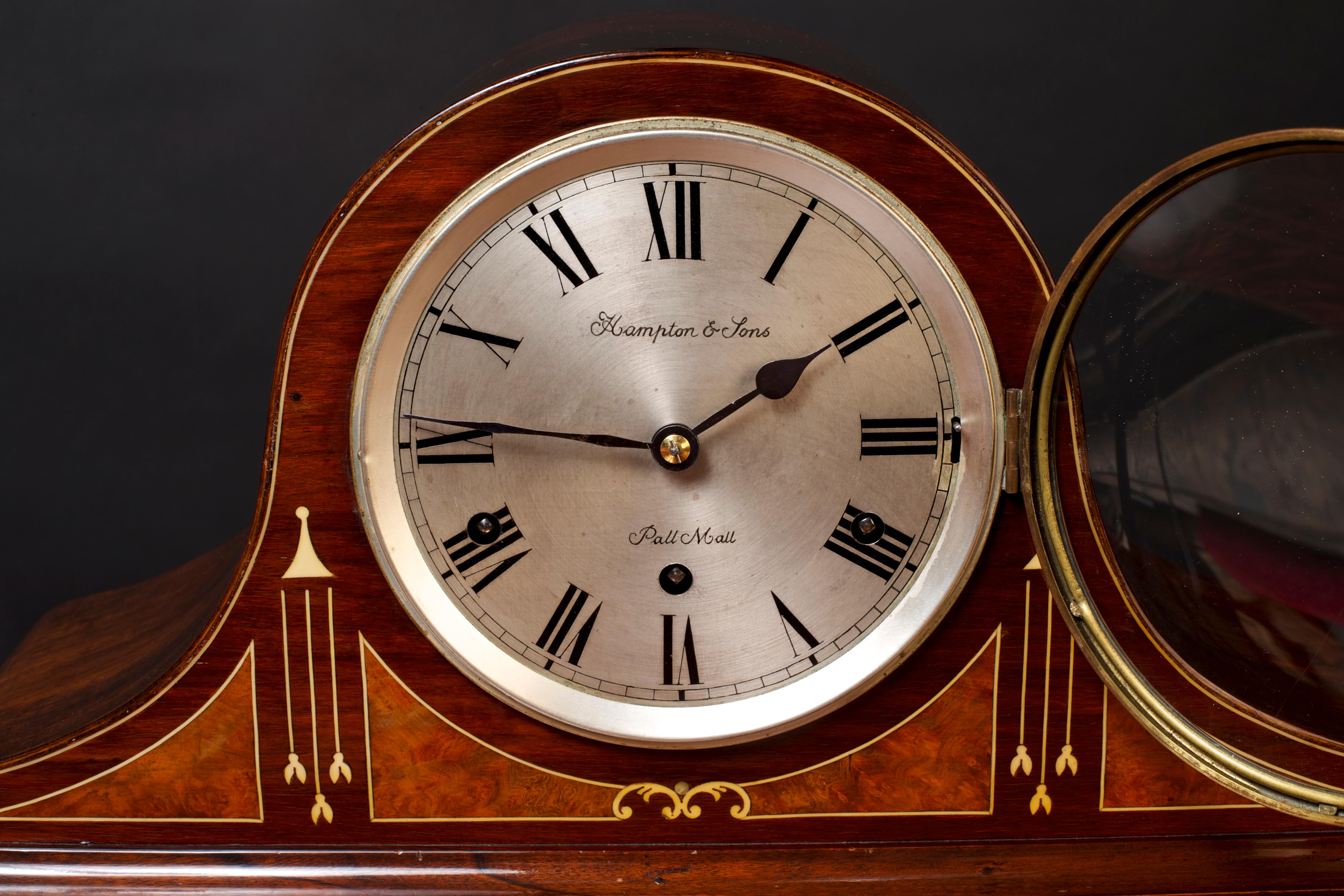 Edwardian mahogany Westminster chiming mantel clock, the case beautifully inlaid with burr walnut quadrants and boxwood line stringing and standing on shallow brass feet. Brass bezel, silvered dial with Roman numerals signed ‘Hampton & Sons, Pall