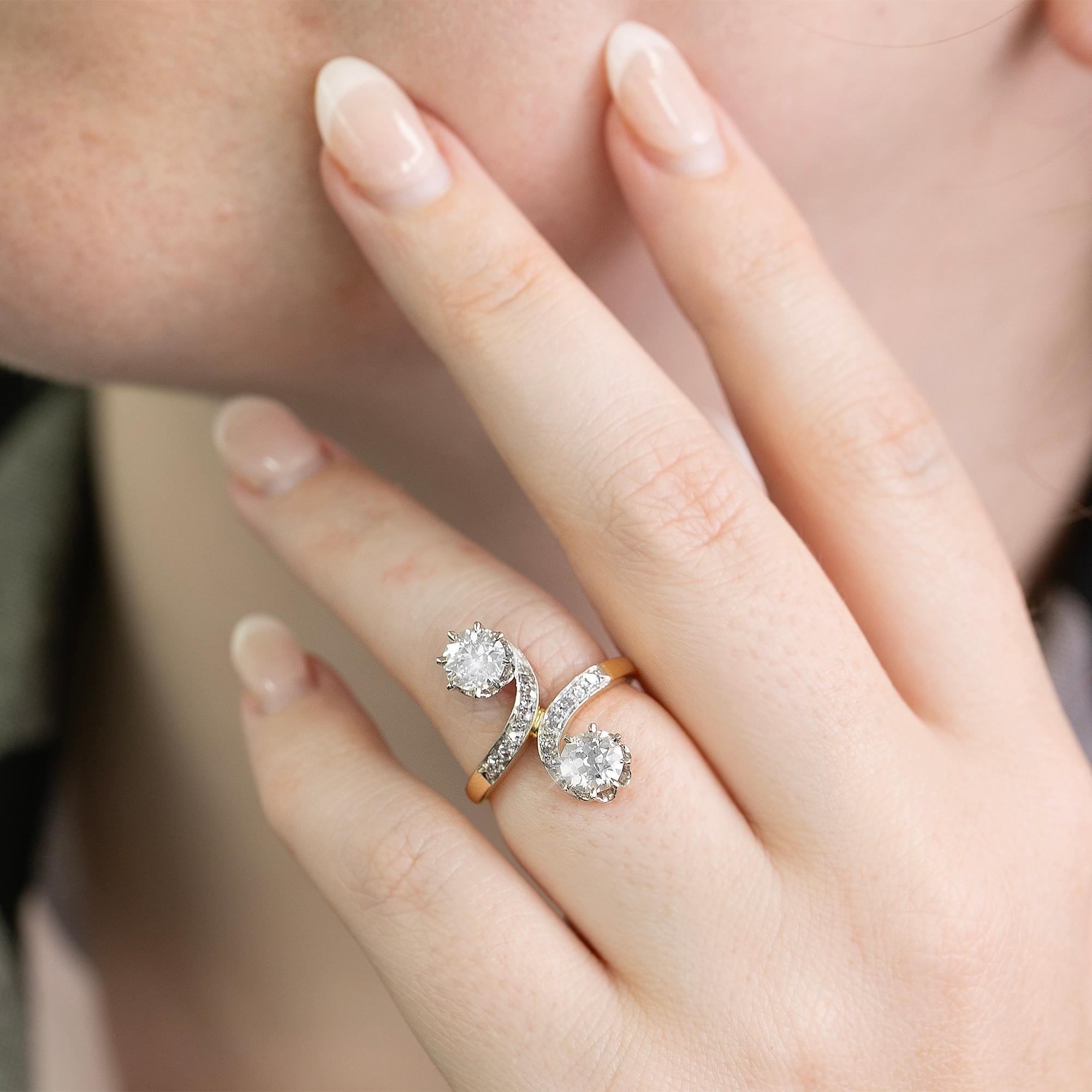 Questo splendido anello edoardiano realizzato in oro giallo e platino presenta delle volute di diamanti incastonati che conducono ai primi diamanti di taglio europeo in raffinate incastonature a griffe. Le pietre caratteristiche sono incastonate in