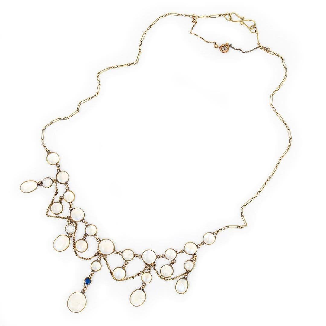 A beautiful Edwardian 9ct gold moonstone necklace comprising 25 oval moonstones of various sizes set in a rubbed over setting with a faceted  sapphire drop to complete this antique festoon. A delicate design with gold festoon links, displaying