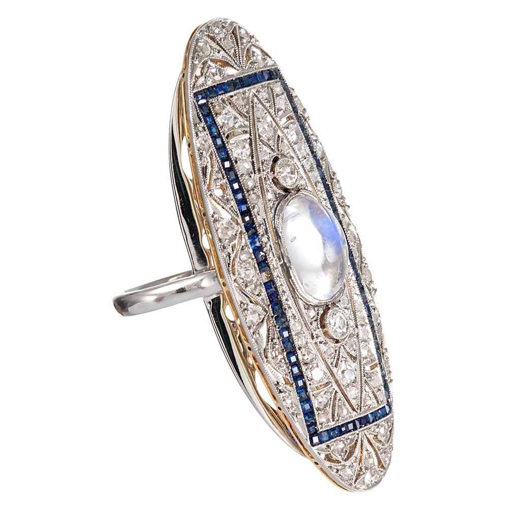 This classically styled Edwardian brooch has been refashioned to a plaque ring. The hand-made ring mounting is platinum and the original brooch is platinum over yellow gold. The center is set with a blue flash cabochon moonstone, it’s mystical color