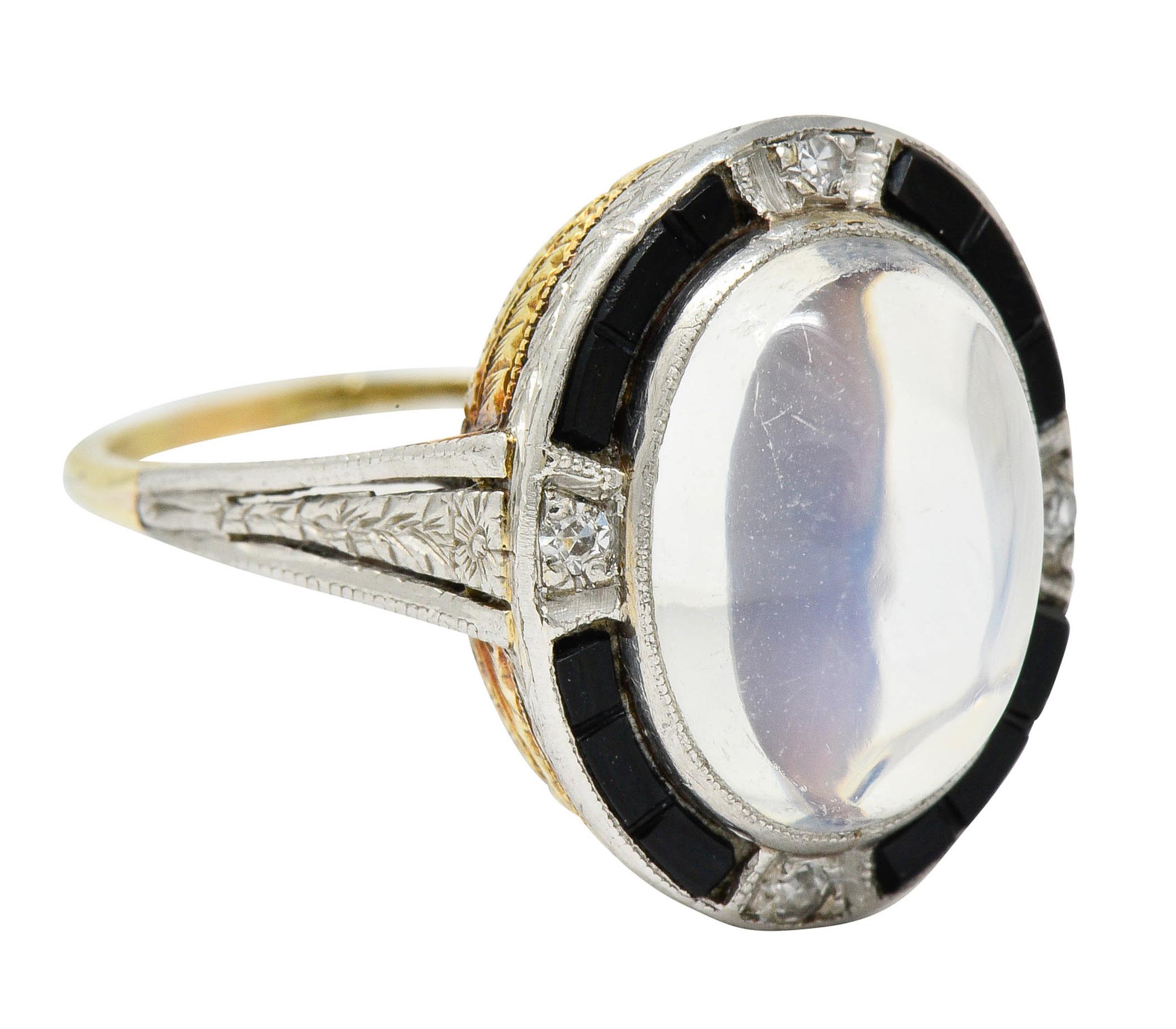 Centering an oval moonstone cabochon measuring approximately 11.6 x 8.7 mm

Translucent with strongly billowing blue adularescence and surrounded by a calibré cut onyx halo

Accented by single cut diamonds, bead set at each cardinal point, weighing