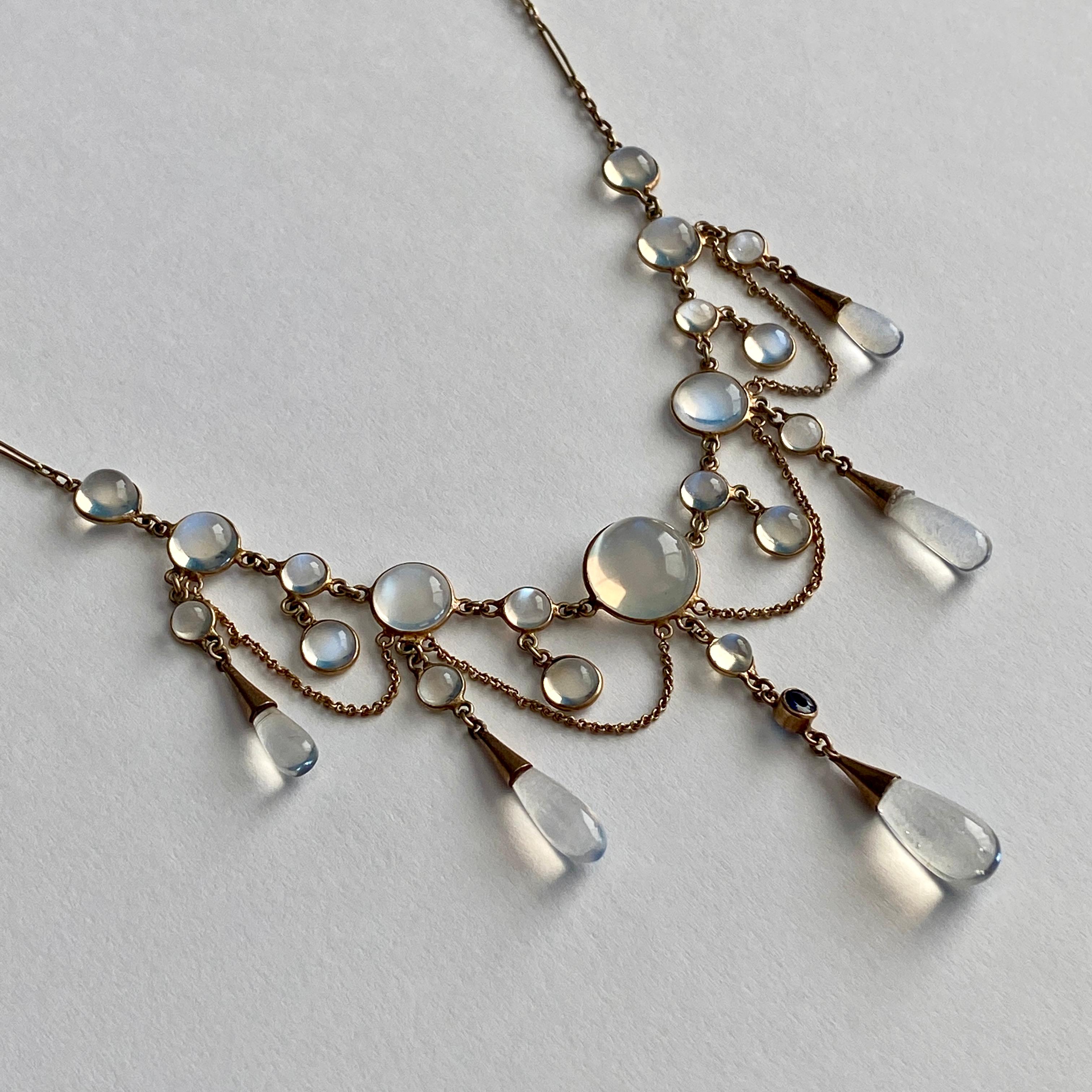 Details:
Sweet Edwardian Moonstone festoon necklace set in 9K yellow gold. This necklace has feminine gold drapes gold chain accented with moonstone drops, and a sweet natural blue sapphire in the center. The moonstones have a nice blue flare, and