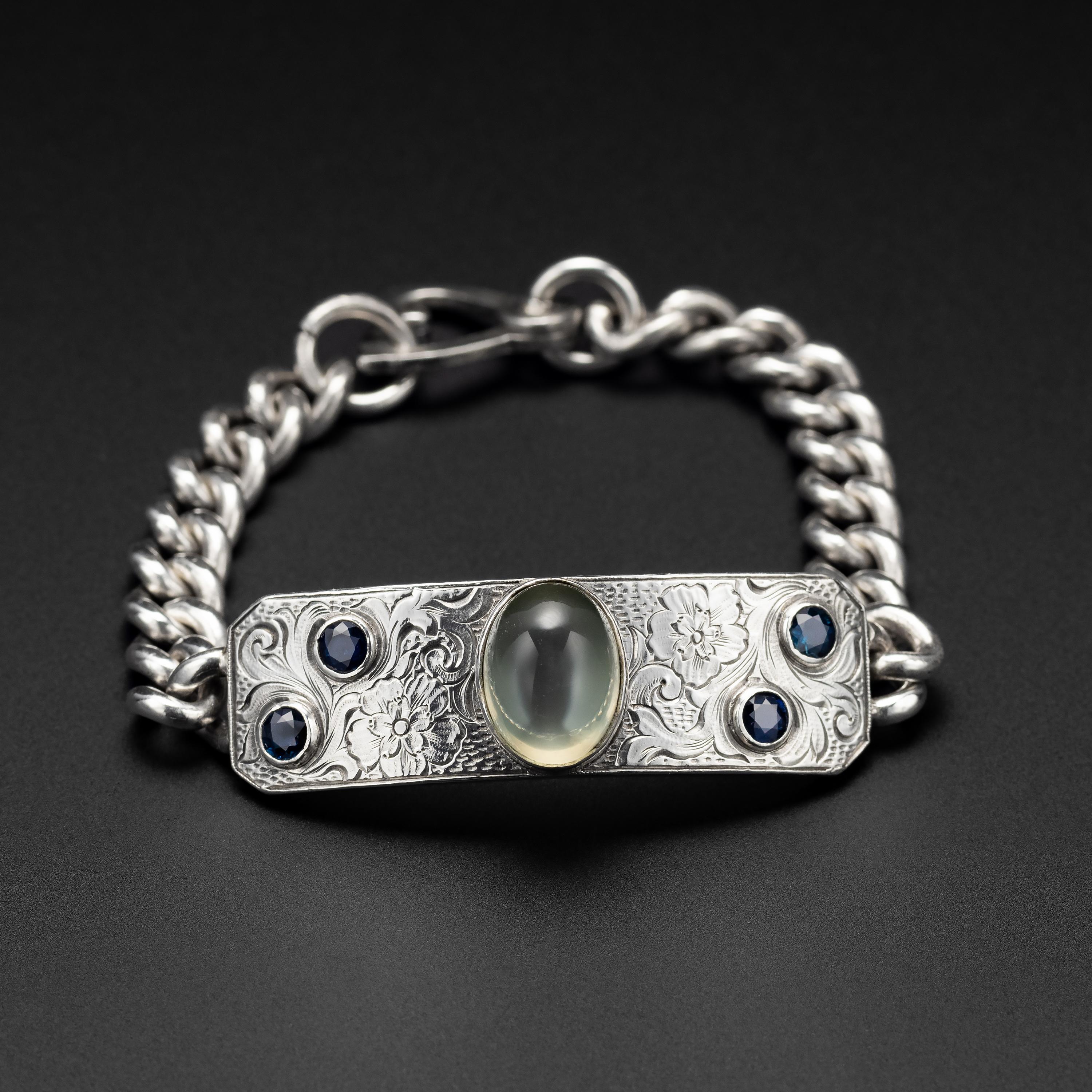 What a beautiful and unusual Edwardian-era (circa 1910) heavy silver bracelet. The thick (2.8mm) curved bar of silver is engraved in a floral motif. In the center is a large and luminous natural moonstone gem. The moonstone measures 14.68mm x