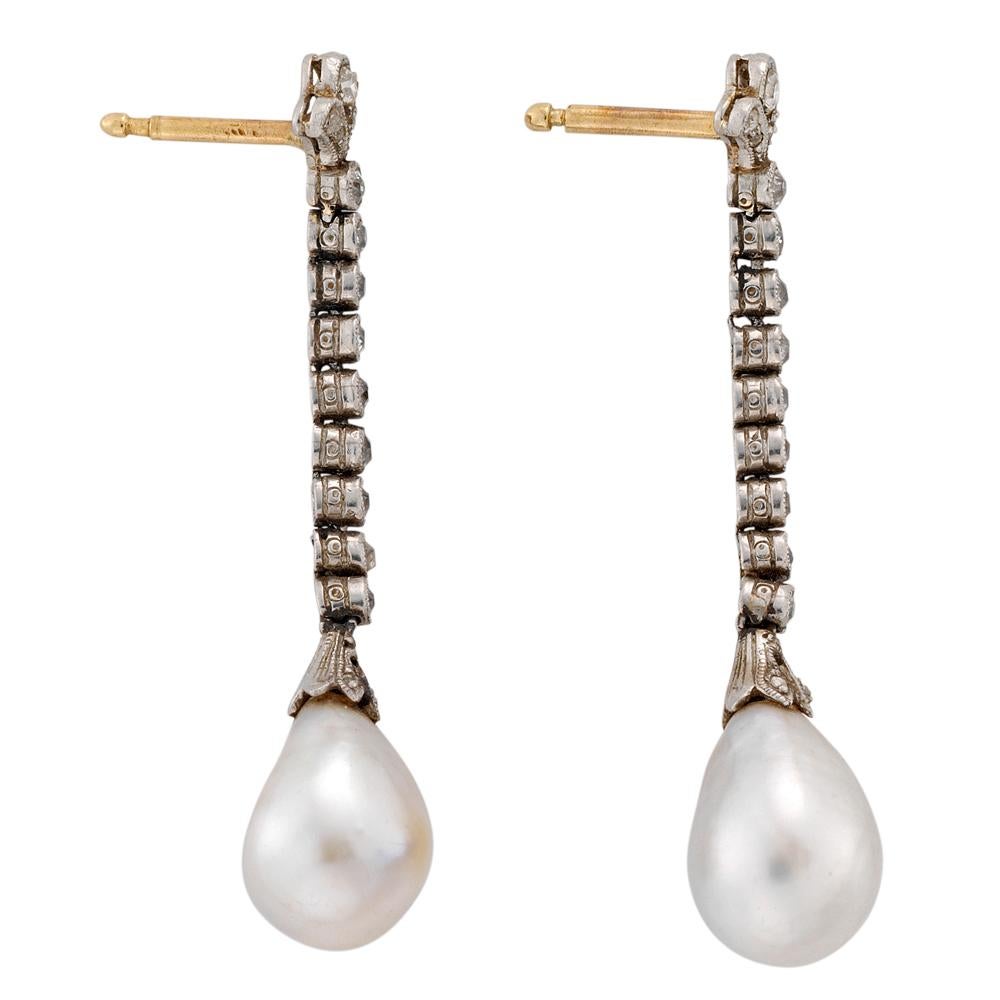 A pair of Edwardian pearl and diamond earrings, the two certificated pear shaped natural pearls measuring approximately 7.65 x 10.75 mm set on a diamond-set cap suspended to a run of nine old brilliant-cut diamonds with stylised fleur-de-lys top,