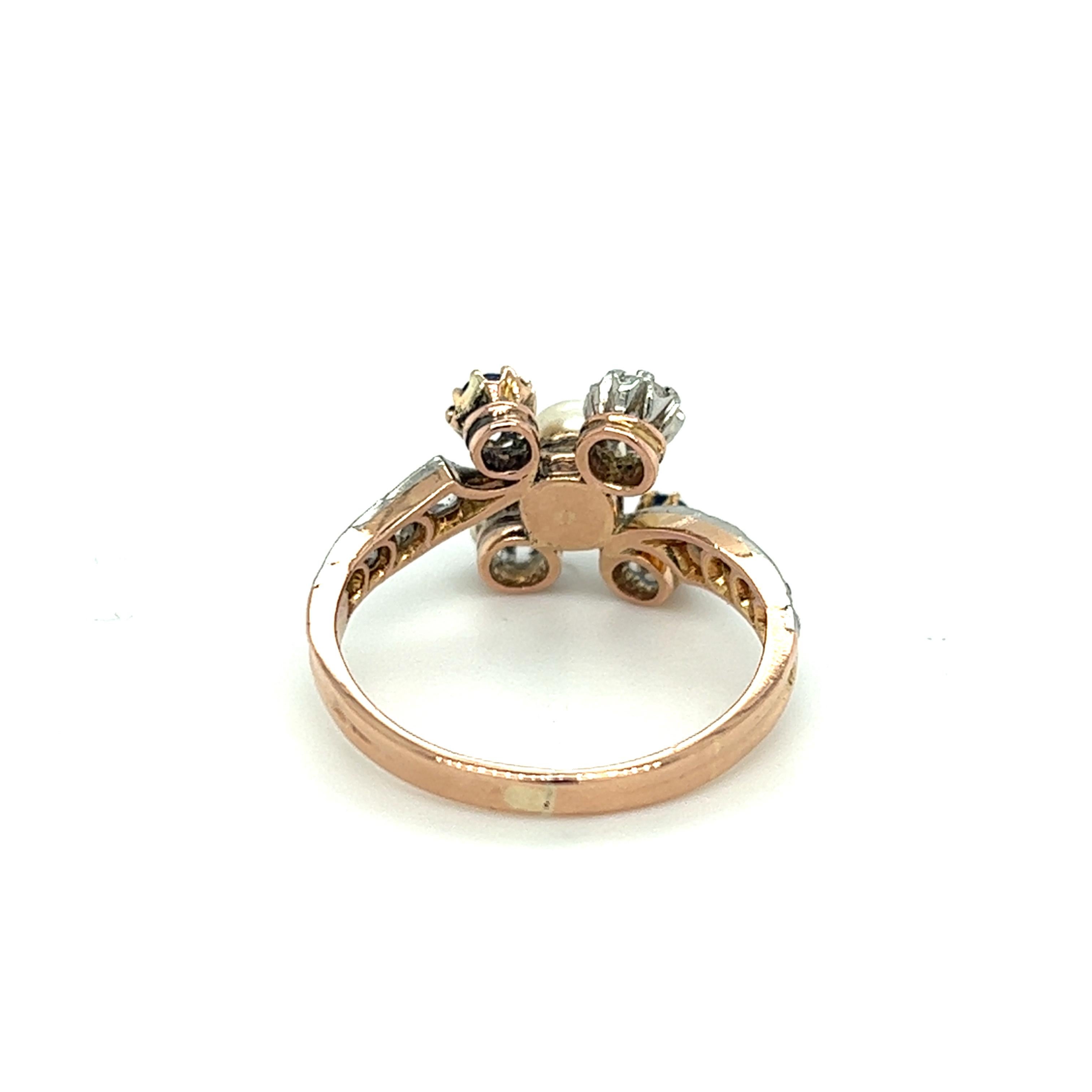 One exquisite 18 karat rose gold and platinum Edwardian bypass design ring set with one 4.5mm cream colored natural pearl, two (2) 2.9mm cushion cut natural blue sapphires, two (2) 2.7mm old mine cut diamonds and eight (8) rose cut diamonds,