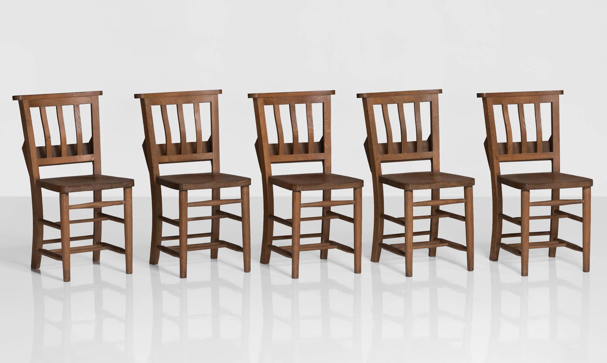 Edwardian oak dining chairs, England, circa 1910.

Solid construction with beautiful joinery details and storage on the back. Originally used in a school house.