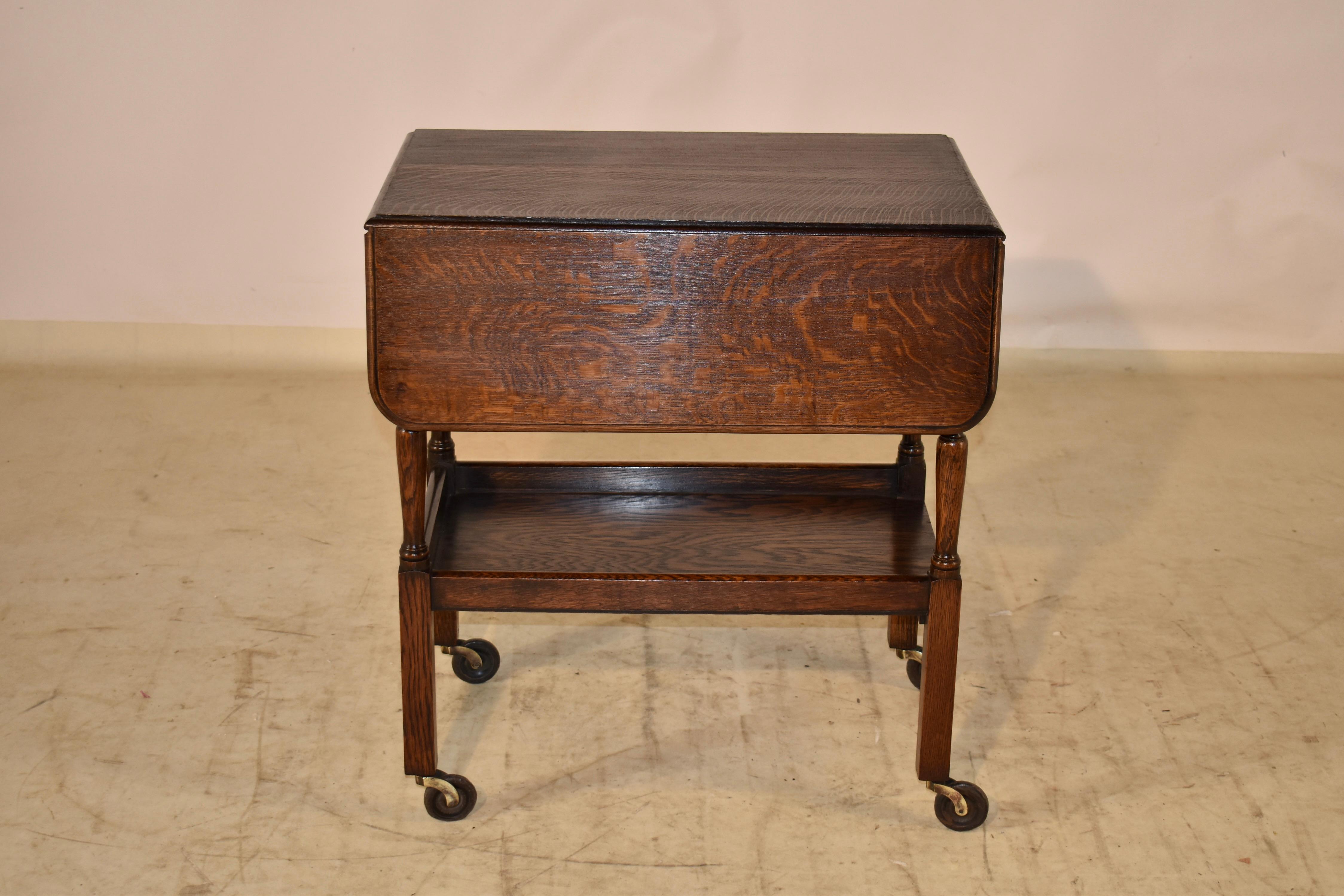 circa 1900 oak drink cart from England. The top has a beveled edge and two leaves. The leaves lift and turn to extend the table to Measure 33.5 inches x 26 inches when the leaves are up. The top has lovely graining and is supported on hand turned