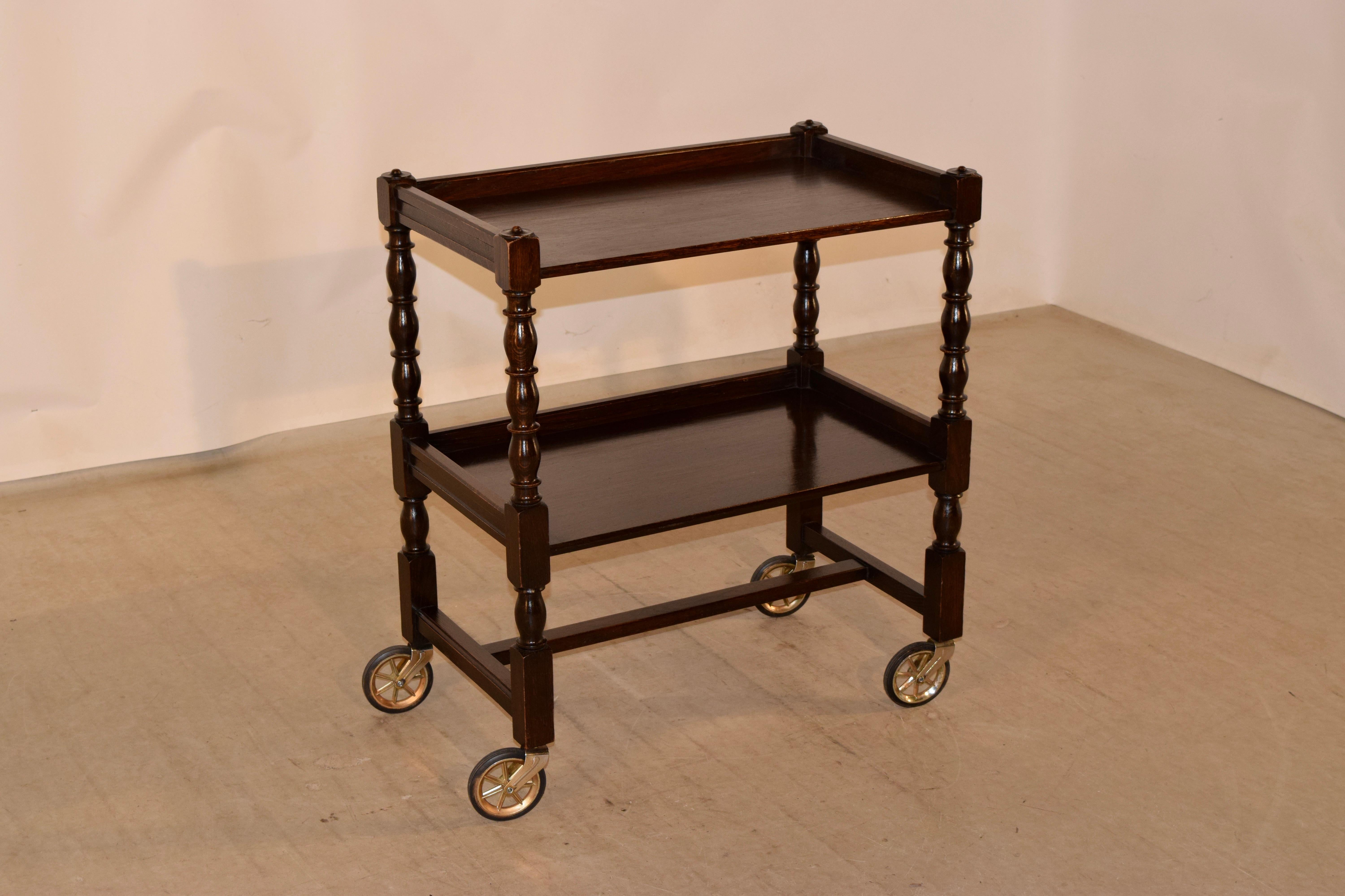 Circa 1910 English oak drinks cart with two shelves, both with galleries surrounding them and separated by hand turned bob and stop shelf supports. The legs are also hand turned and are joined by simple stretchers and supported on oversized wheels