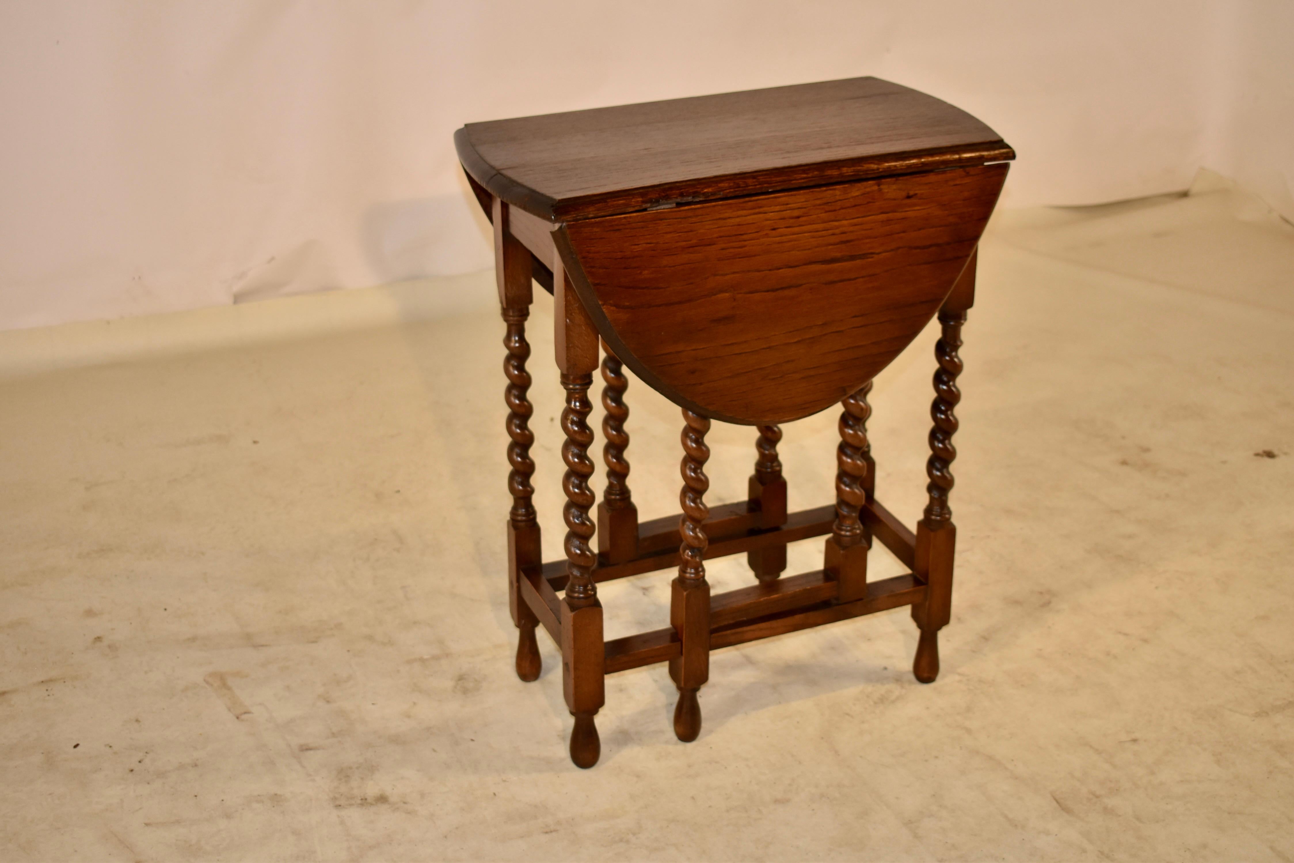 Edwardian oak side table from England with two gate legs. The top has a beveled edge and follows down to simple aprons and supported on hand turned barley twist legs and gate legs. The legs are connected with simple stretchers and the table is