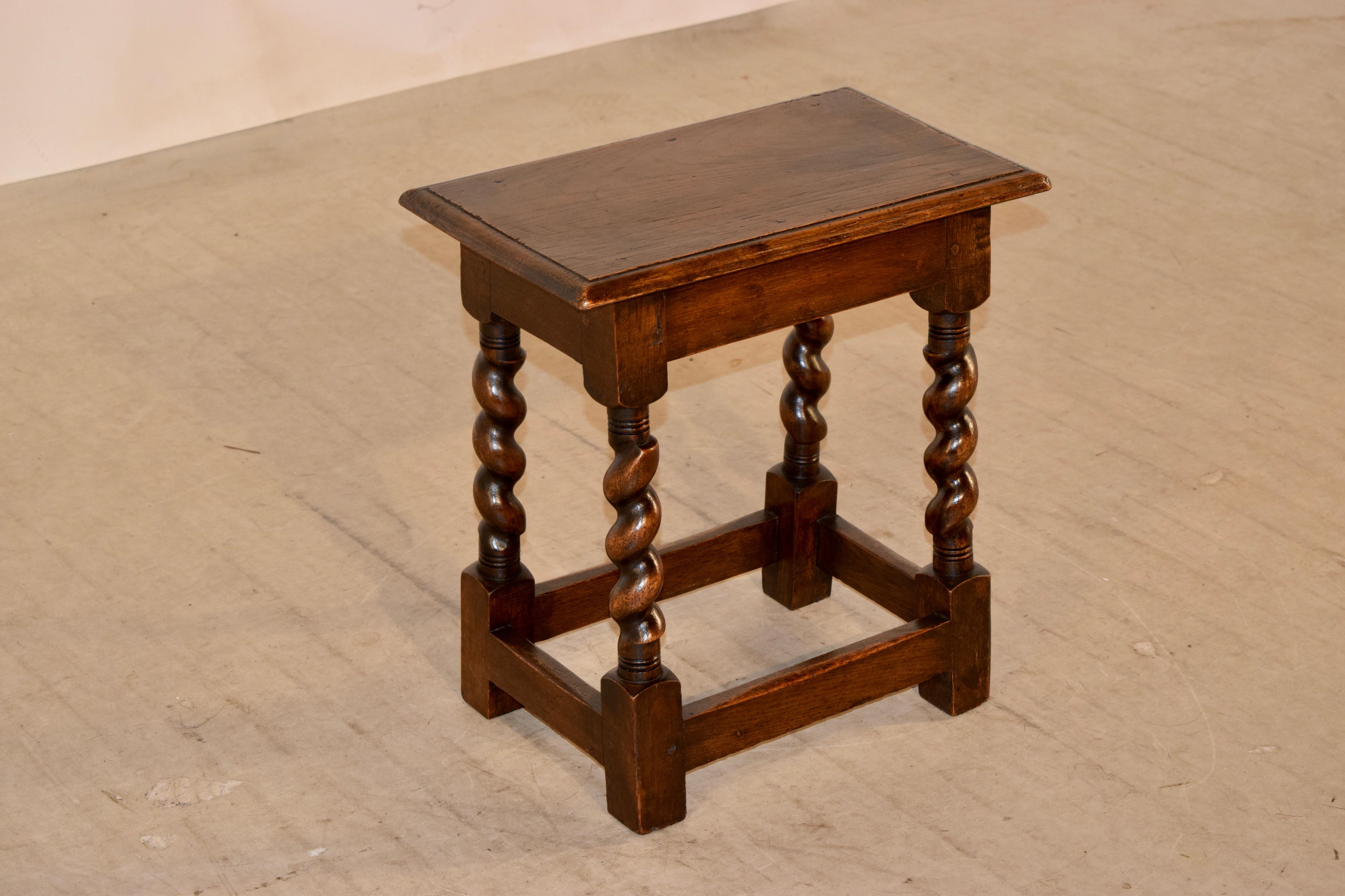 Edwardian English oak joint stool with a beveled edge around the top and simple apron, supported on hand-turned barley twist legs, joined by simple stretchers.