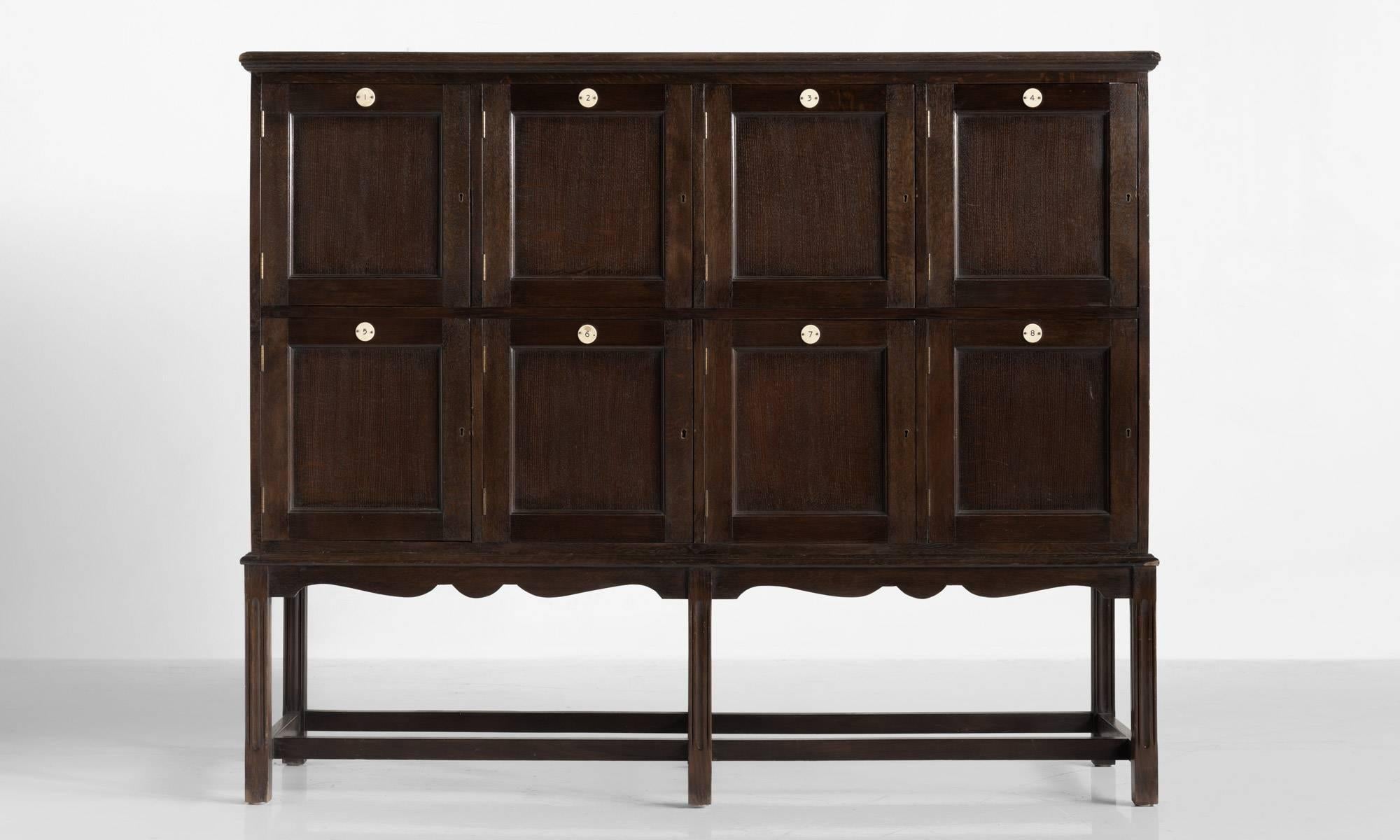 Edwardian oak lockers, circa 1900

Moulded oak top with eight paneled locker doors with numbered circular discs.