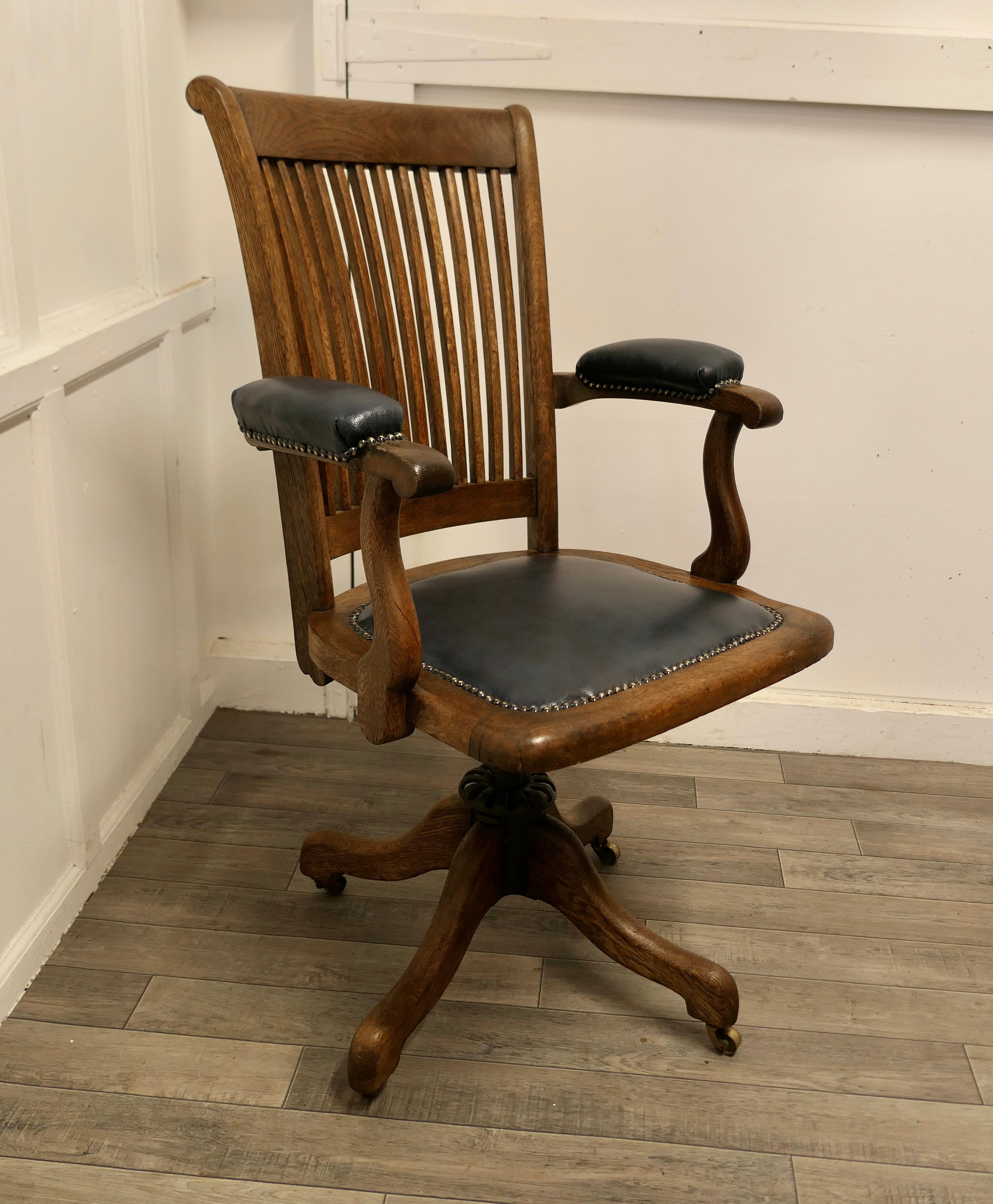 Edwardian oak office or desk chair.

This Art Deco Oak office chair has an attractive curving slatted shaped high back with a wide curved top rail and comfortable upholstered arm rests and seat. The chair tilts and swivels, the height is