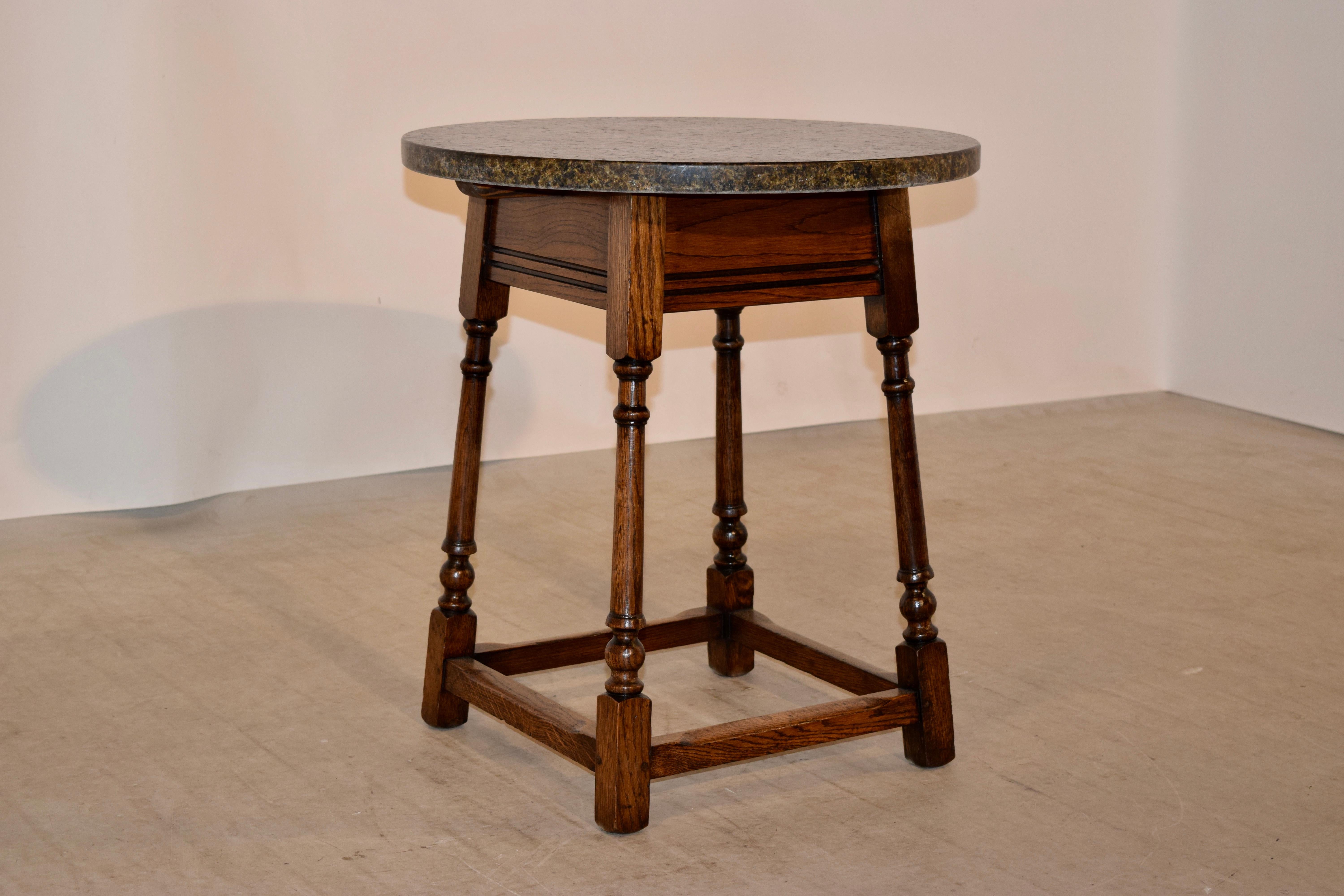 English oak side table with a marble top, circa 1900. The marble has a leathered appearance and is rich in color and depth. The base is hand-turned and has splayed legs joined by simple stretchers.