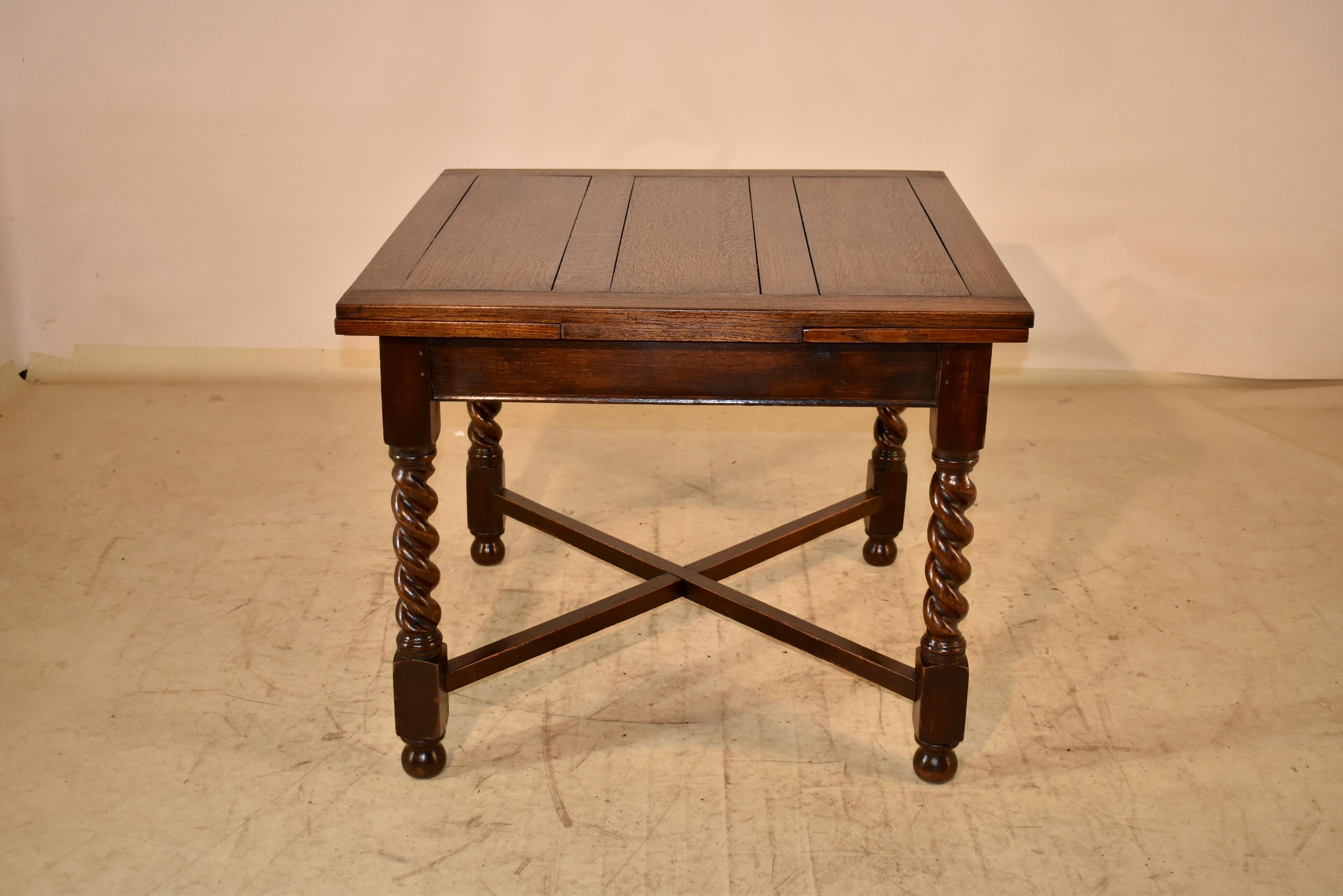 Circa 1900 Edwardian oak dining table with two draw leaves.  The top and leaves are paneled, and are supported on top of a base with a simple apron over hand turned barley twist legs.  The legs are connected by simple cross stretchers and raised on
