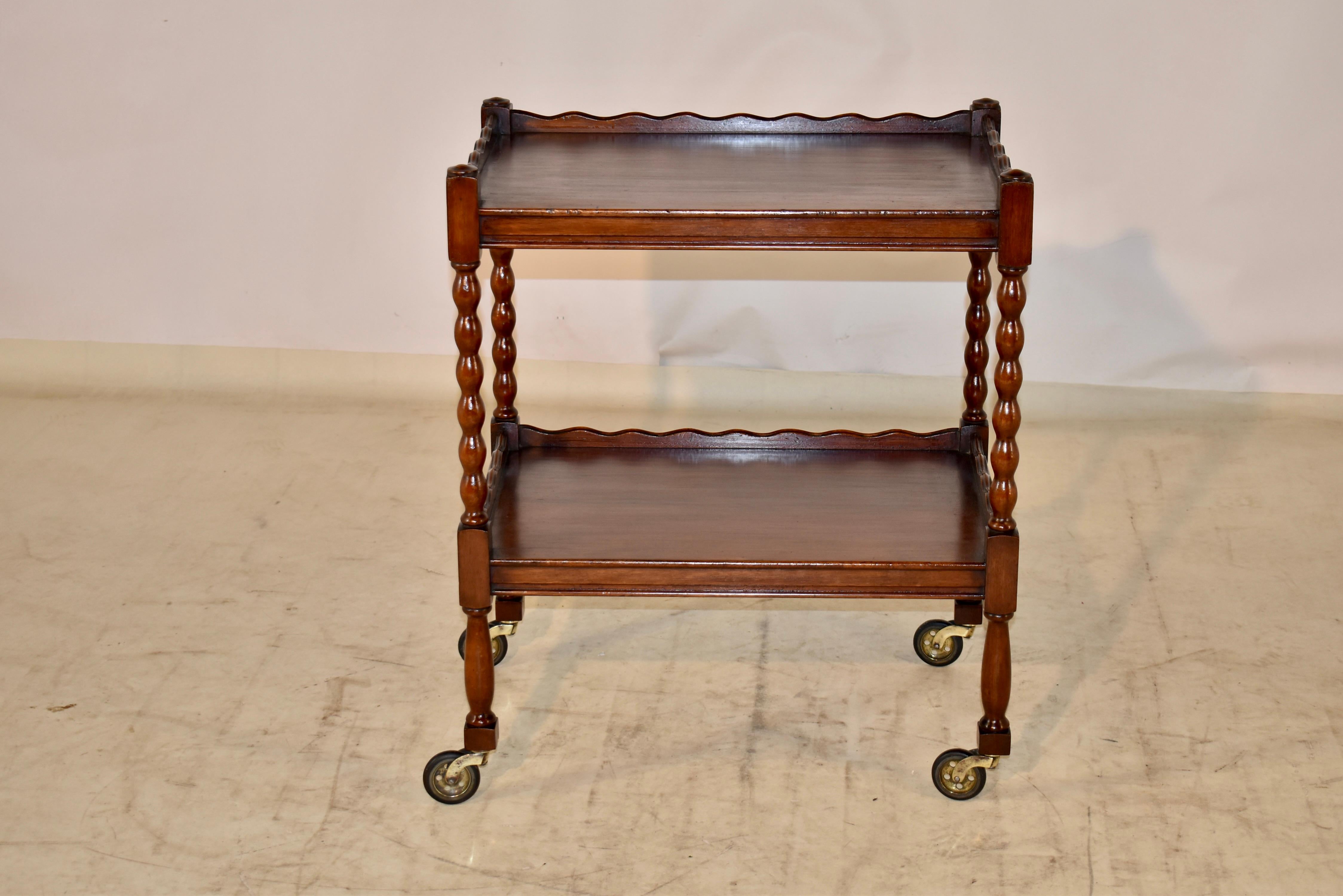 Edwardian oak drinks cart from England. The cart has two shelves, both with hand scalloped galleries on three sides for easy tray removal on the front side. The shelves are separated by hand turned bobbin style legs, and supported on hand turned