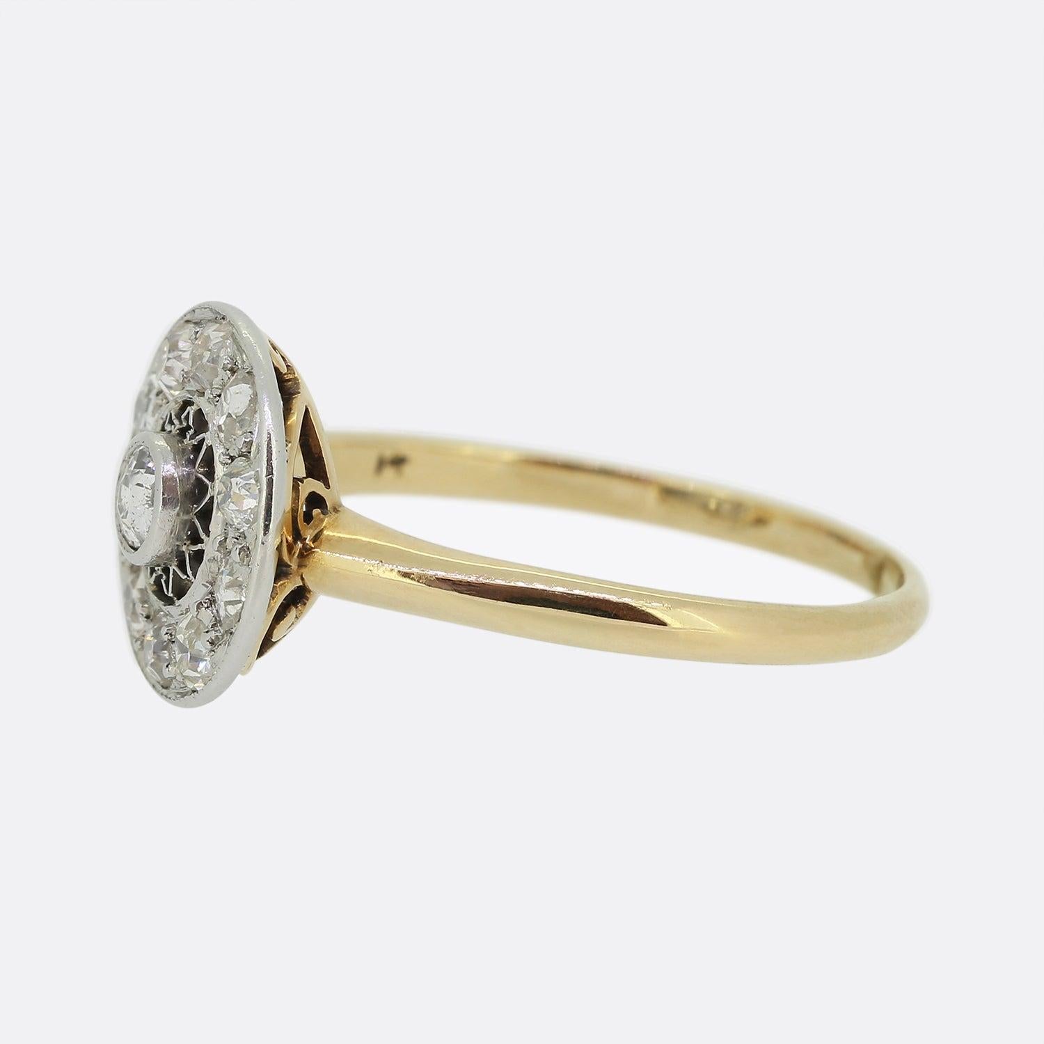Here we have a wonderful diamond cluster ring from the Edwardian era. This piece features a centralised rub-over set round old cut diamond that is surrounded by an open sunburst geometric design. Fine platinum milgrain detailing flows around the
