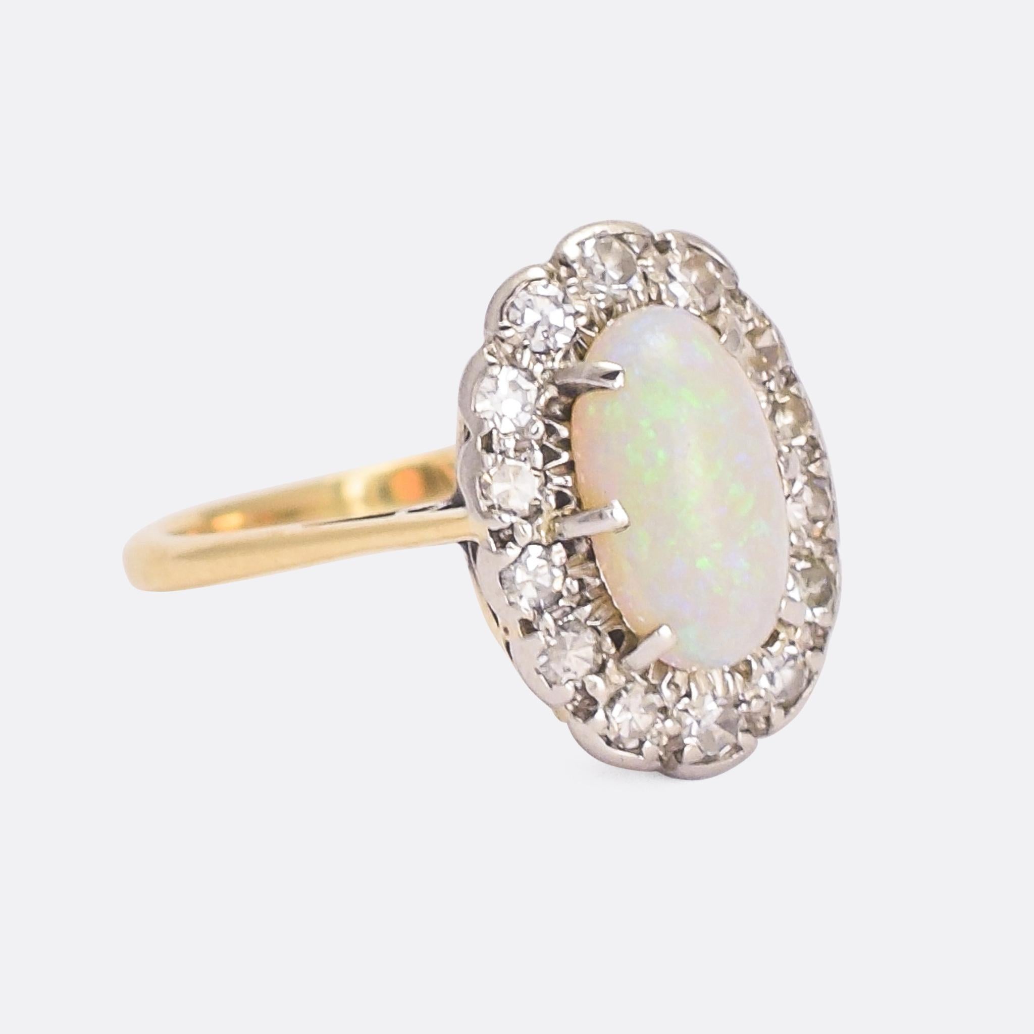 A beautiful antique opal and diamond oval cluster ring dating from the Edwardian era, circa 1910. It's modelled in 18 karat yellow gold with platinum settings, the latter chosen to enhance the colour of the stones. The opal is bright and lively,