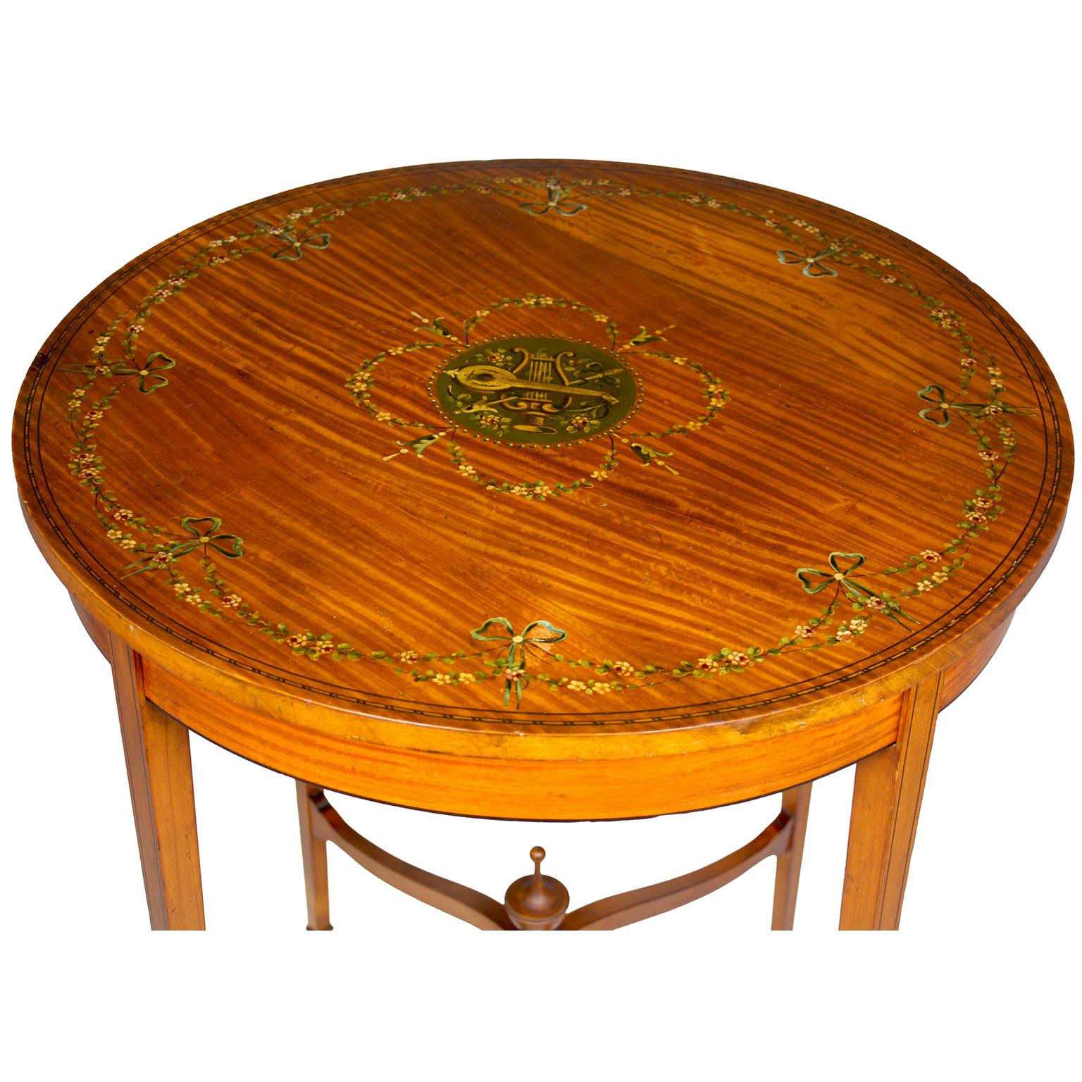 An Edwardian Painted Satinwood Occasional Side Circular Side Table. The Adams Style round table, hand painted with decorations of floral garlands, ribbons and musical instruments, with four tapered legs conjoined and centered with a carved