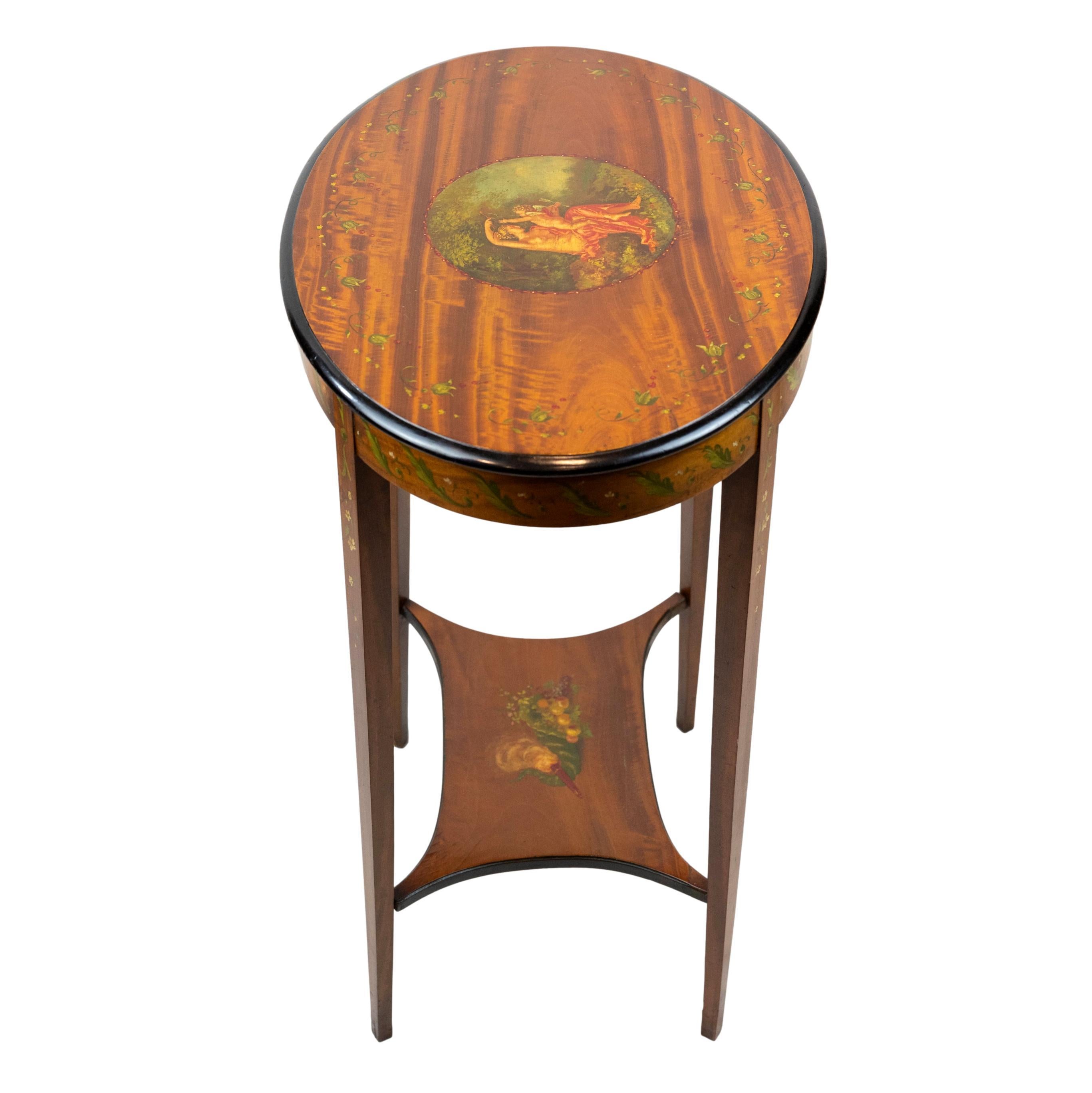 Edwardian Satinwood Two-Tier Occasional Table, the top with a hand-painted classical Roman depiction of Venus taking away her son Cupid's bow, with an ebonized banded edge, the lower shelf hand-painted with a fruit-filled cornucopia and fan, with