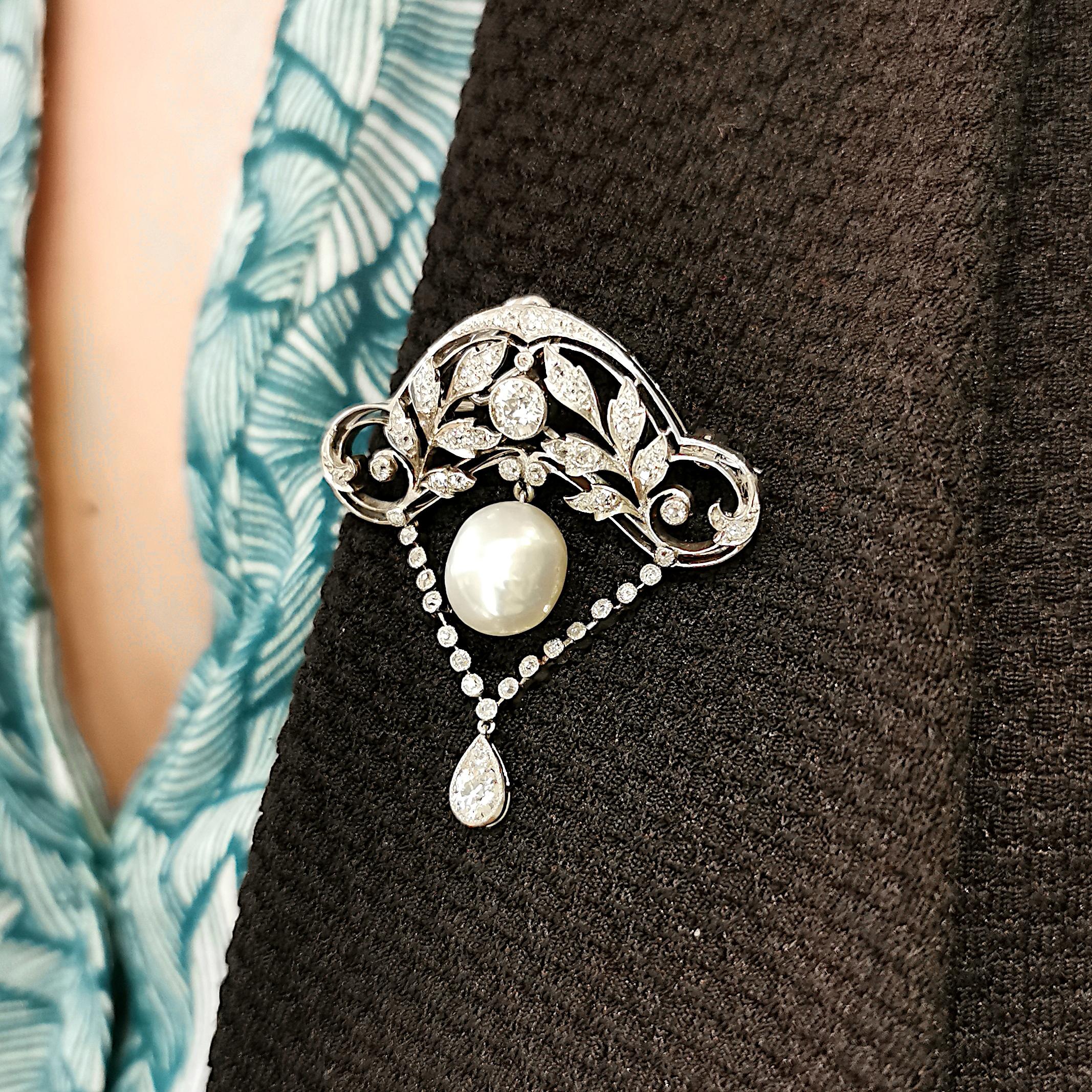 A fine Edwardian, natural pearl and diamond brooch-pendant, with an old-cut diamond, flanked by leaf motifs, in an open work, curved, Art Nouveau influenced frame, with a natural pearl pendant suspended from the centre, with a row of old-cut