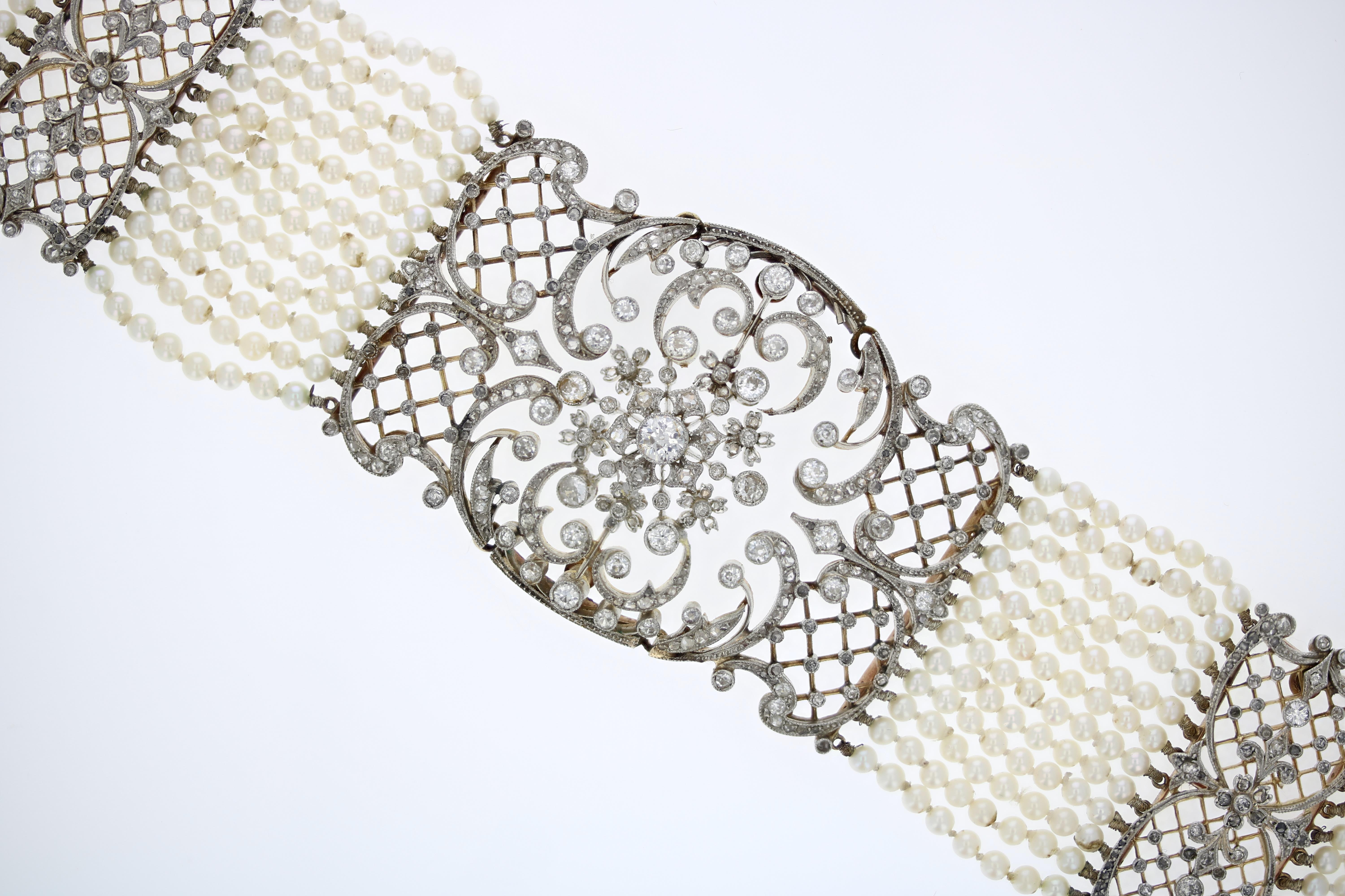A finely crafted Edwardian era collar necklace with 12 strands of seed pearls interspersed with three stations of diamond medallions. The diamonds are European-cut and set in intricate floral filigree metalwork of platinum and yellow gold.